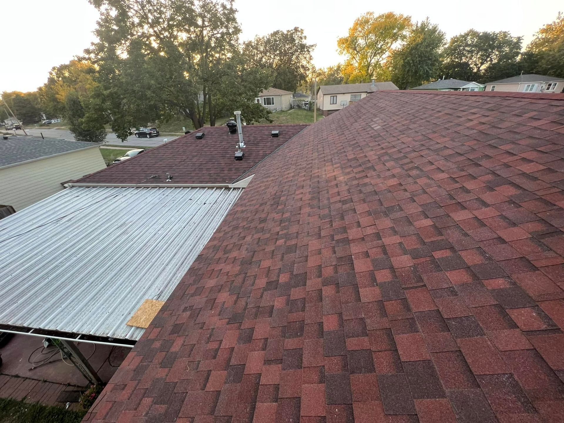 Roofing work on a house, showing a new red shingle roof beside a corrugated metal section.
