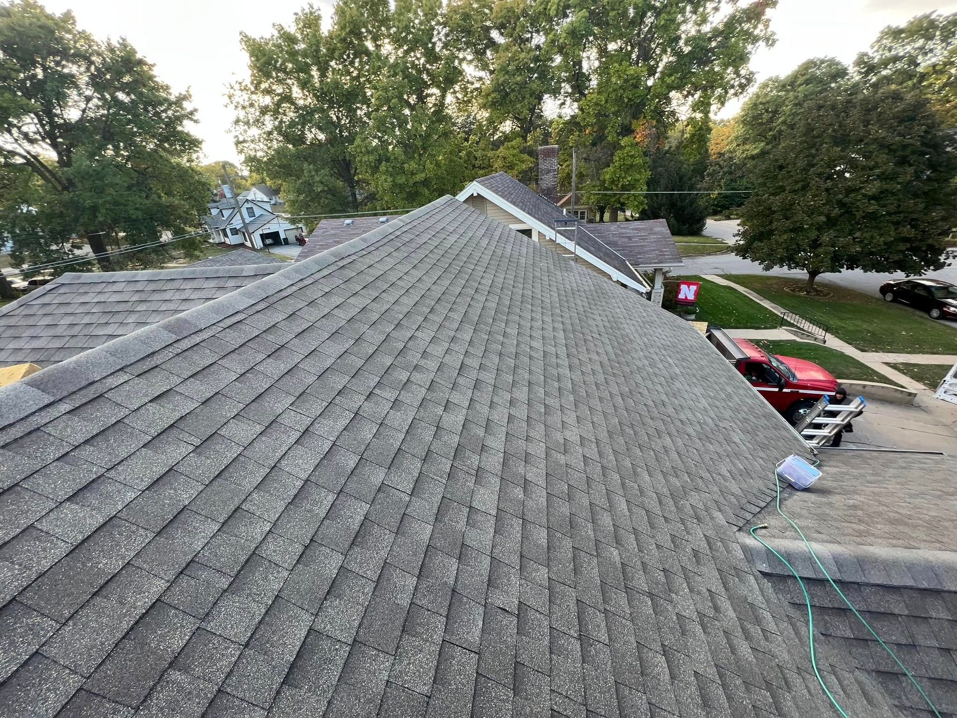 Roof shingles viewed from above, with trees and parked cars in a suburban neighborhood.