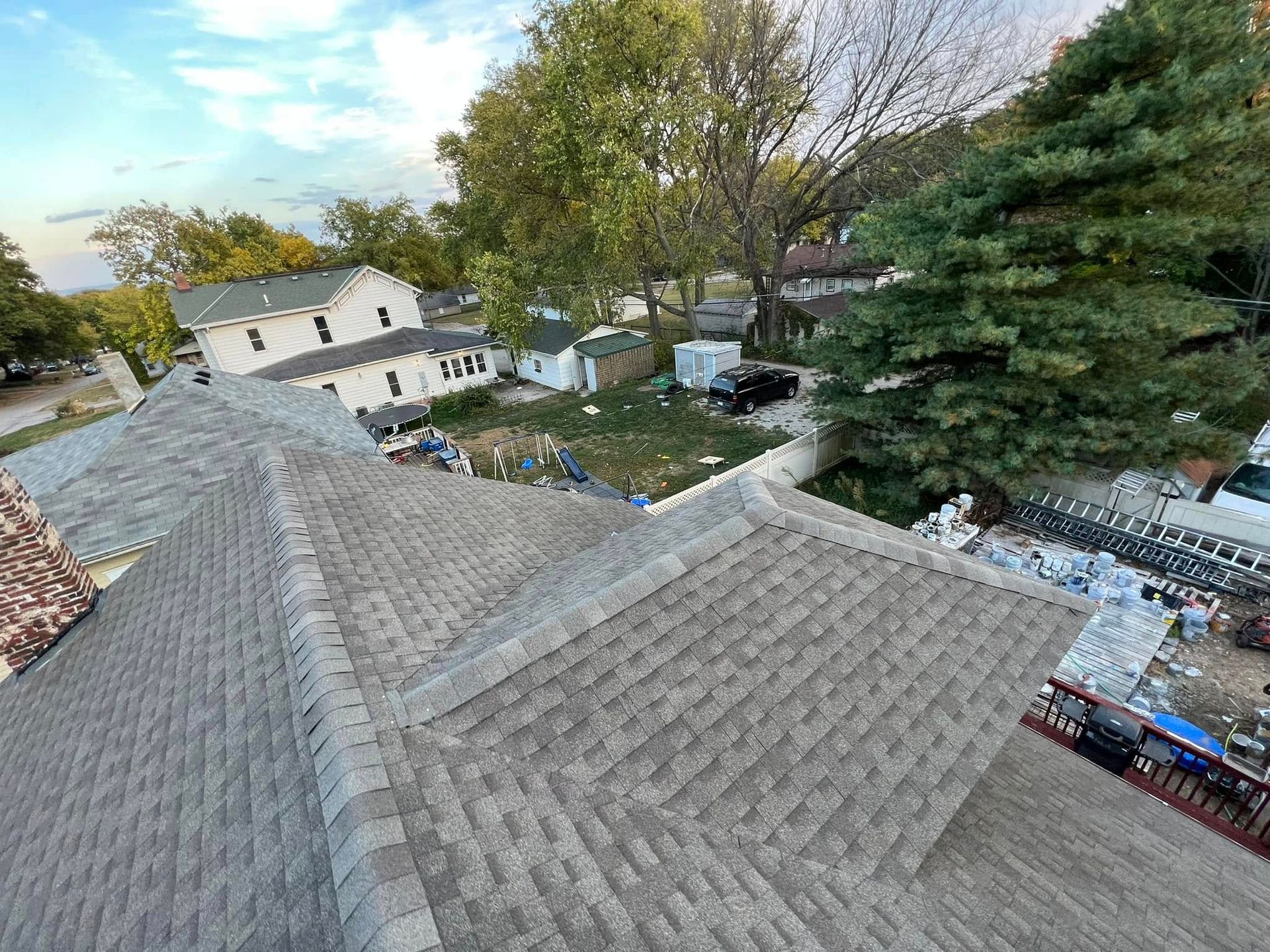 Rooftop view of a suburban neighborhood with gray shingles, trees, and houses below
