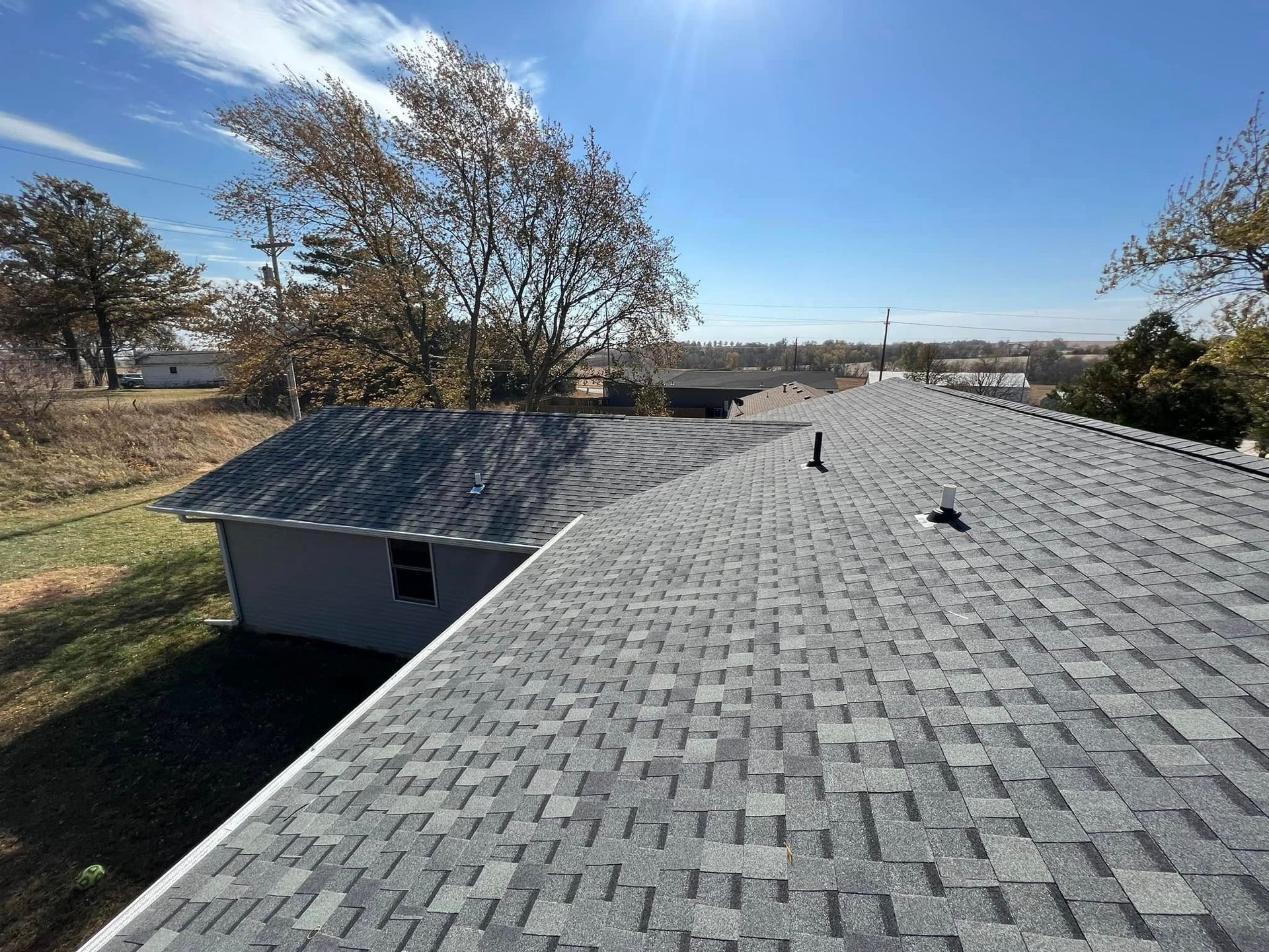 Gray shingled roof with vent pipes under a clear blue sky on a sunny day