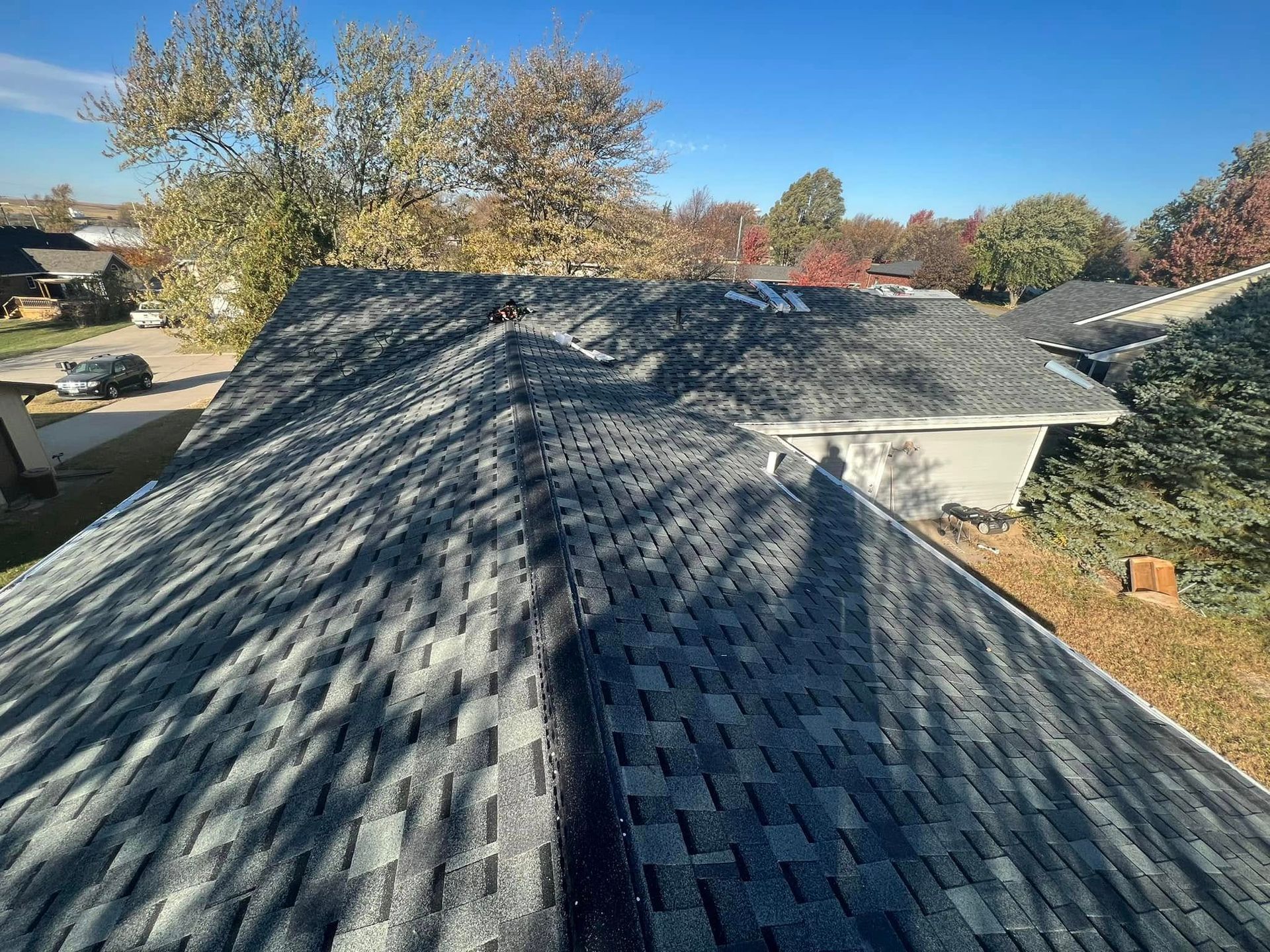 Roof shingles on a house under a clear blue sky, with tree shadows across the roof.
