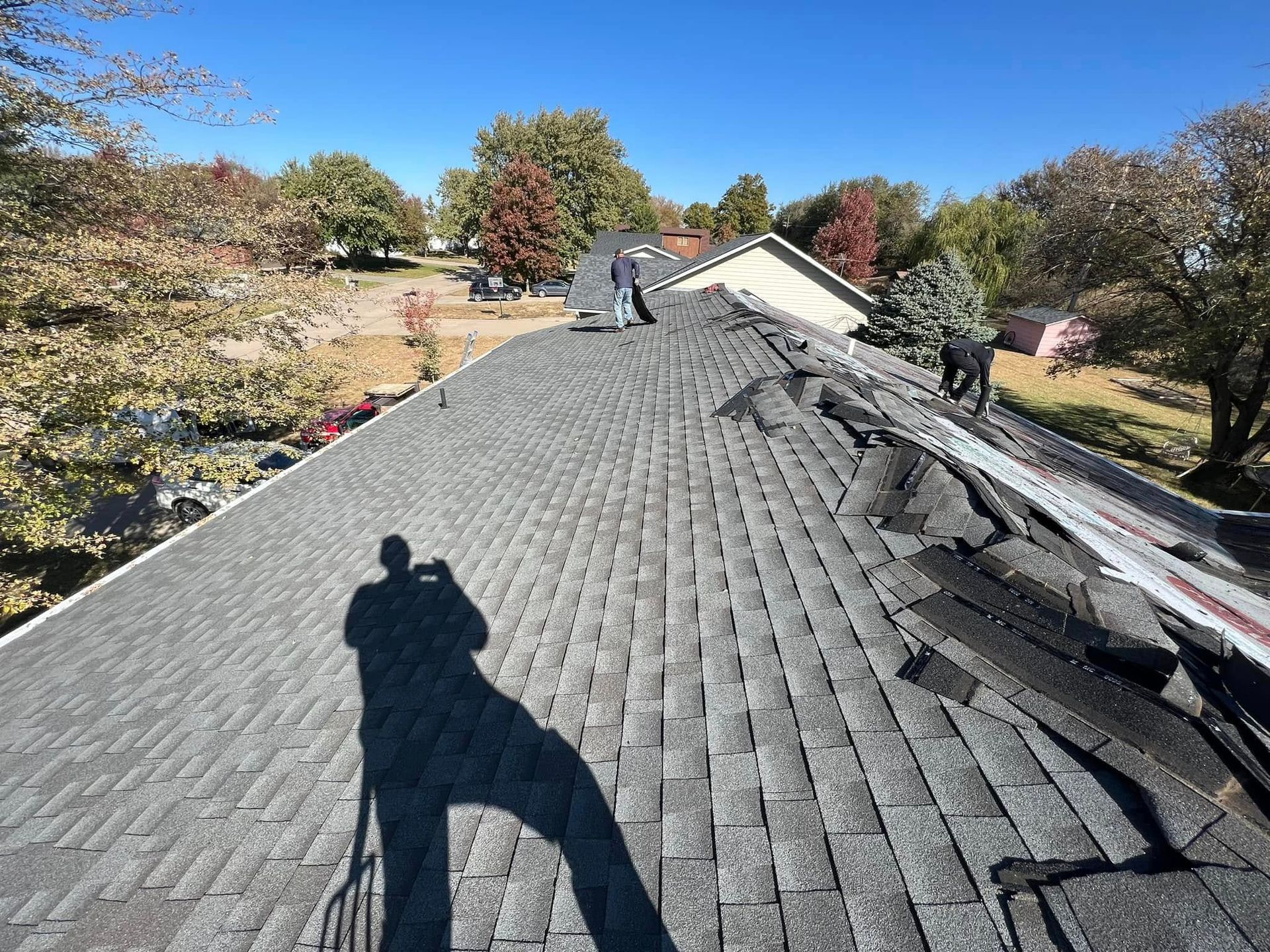 Roof workers repairing a shingled roof on a house in autumn