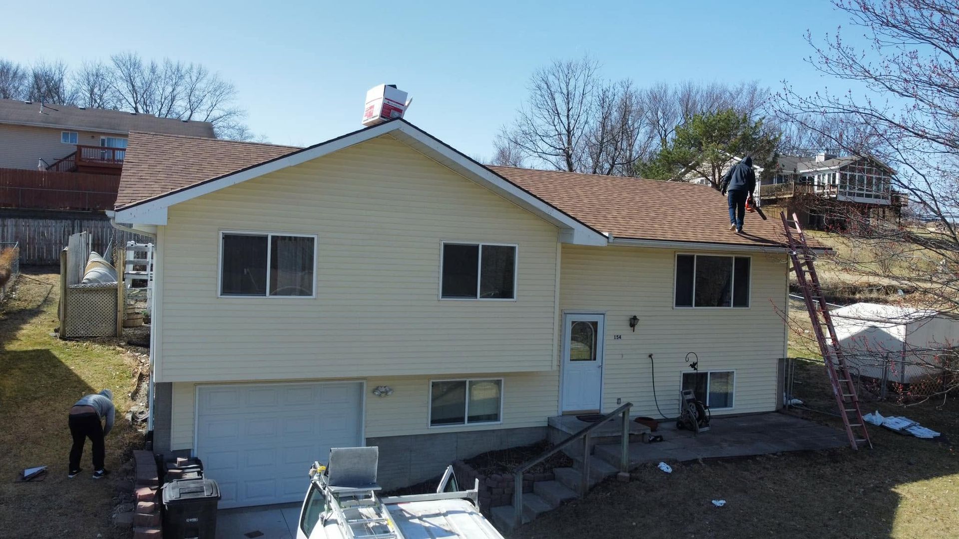 Yellow house with workers on the roof and ground, showing exterior repair or construction work