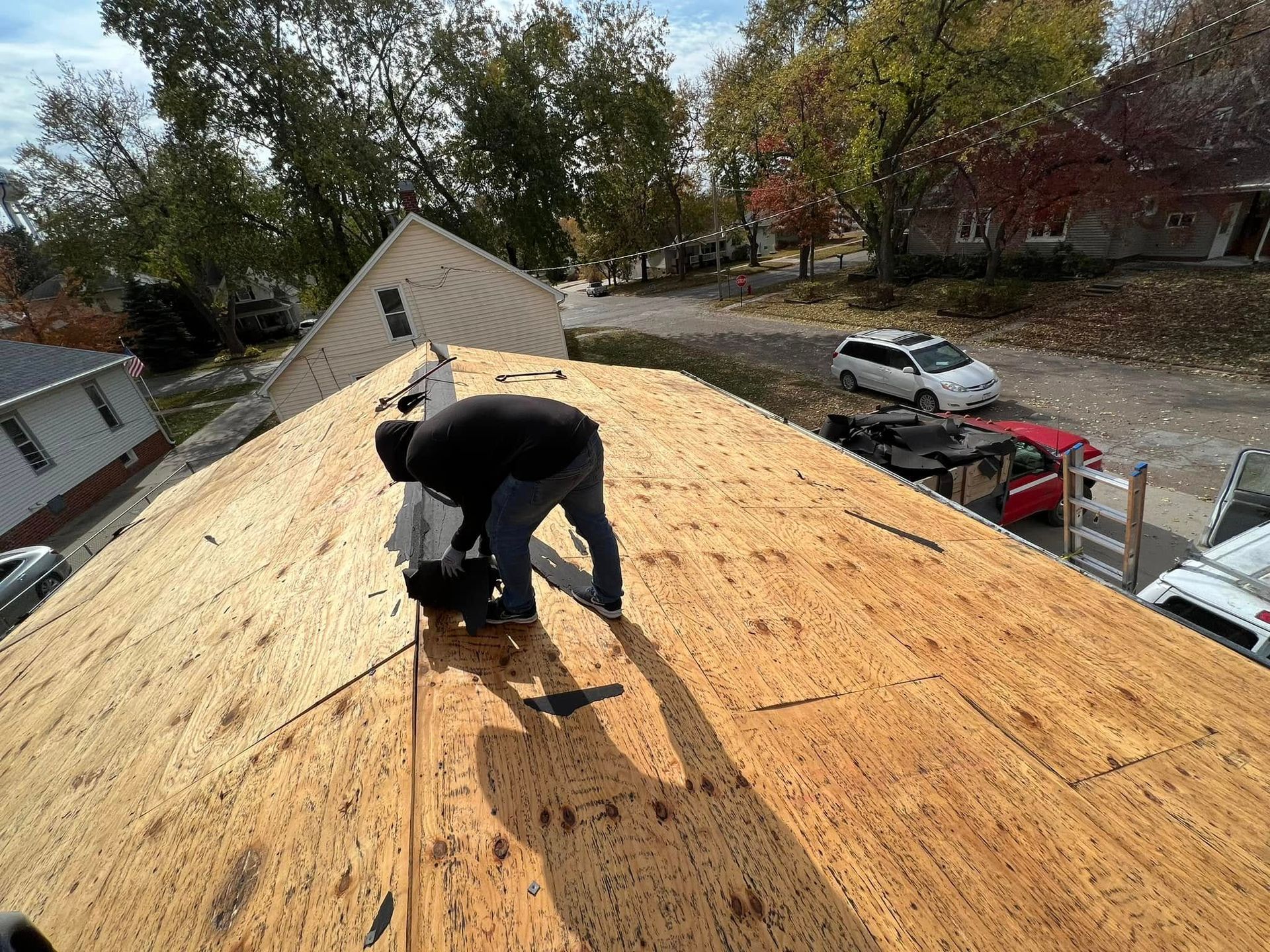 Worker kneeling on a roof, installing plywood sheathing on a sunny residential house.