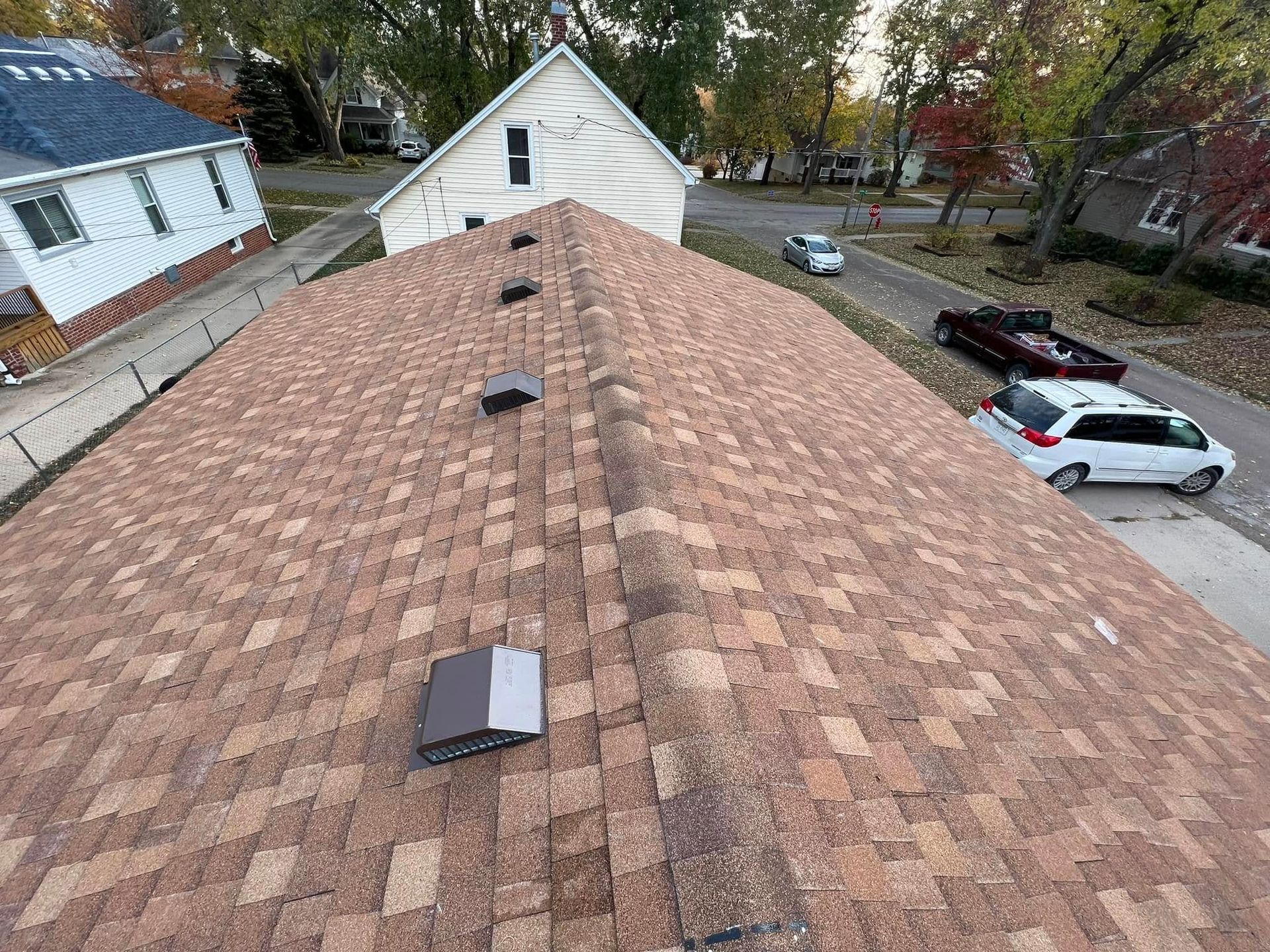 Aerial view of a shingled house roof with skylights in a suburban neighborhood.
