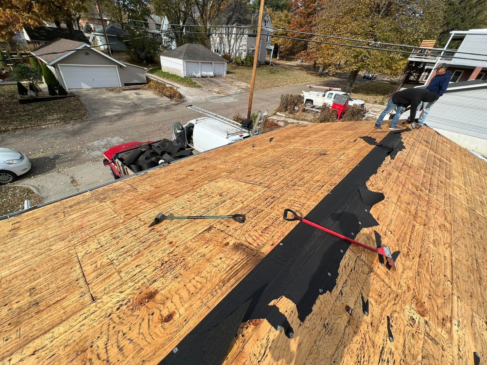 Roof under repair with new black underlayment and tools on plywood sheathing, viewed from the roof ridge