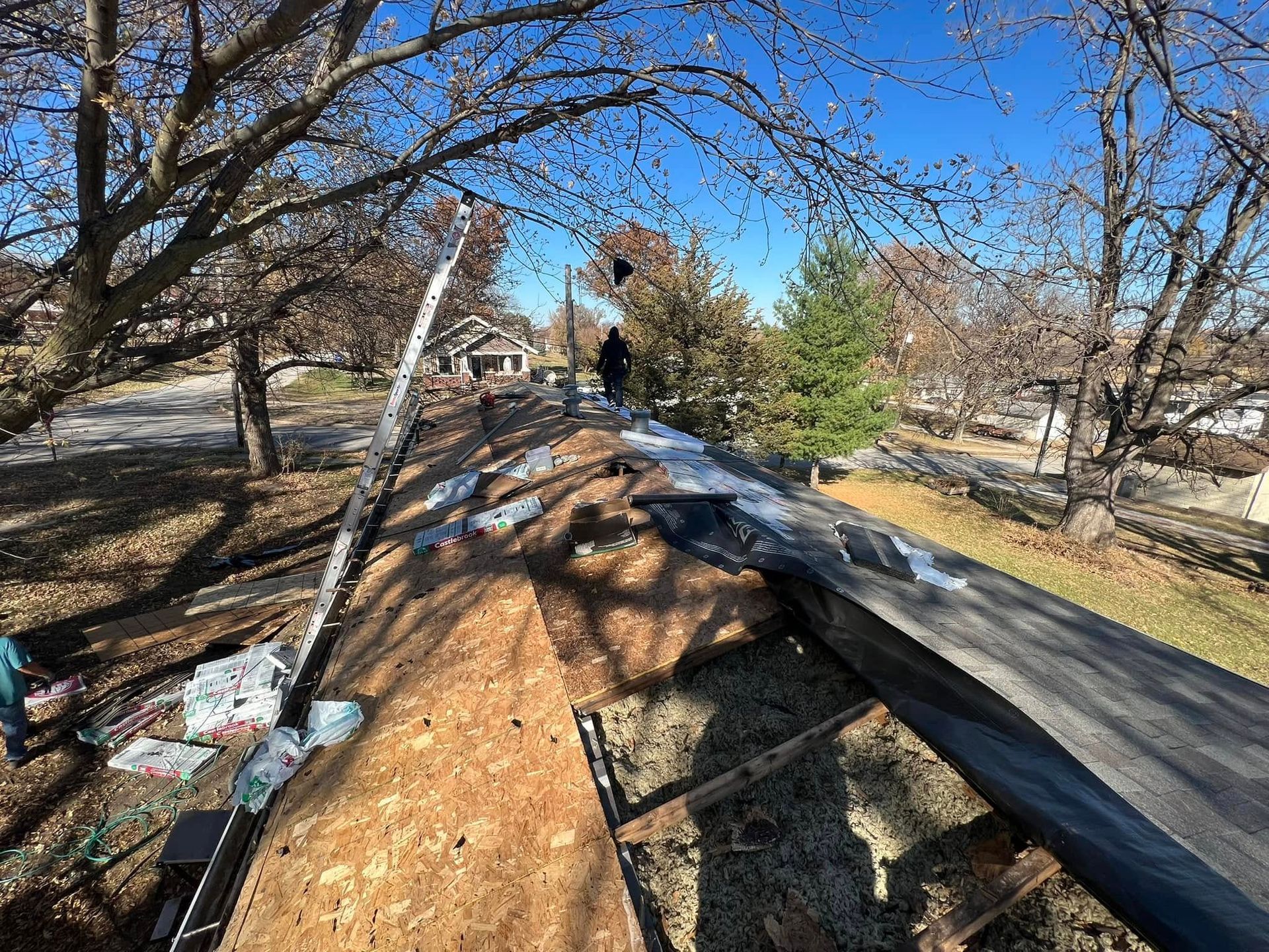 Roof under construction with black shingles, wood framing, and trees in the background
