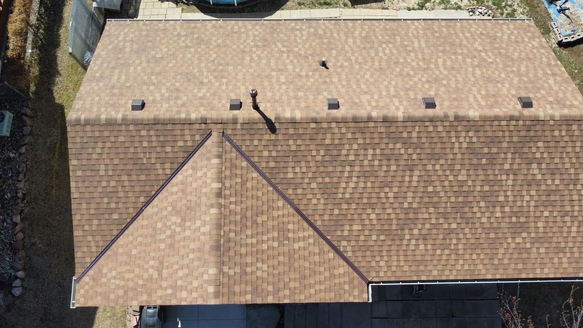 Aerial view of a tan shingle roof with vents and a triangular front section.