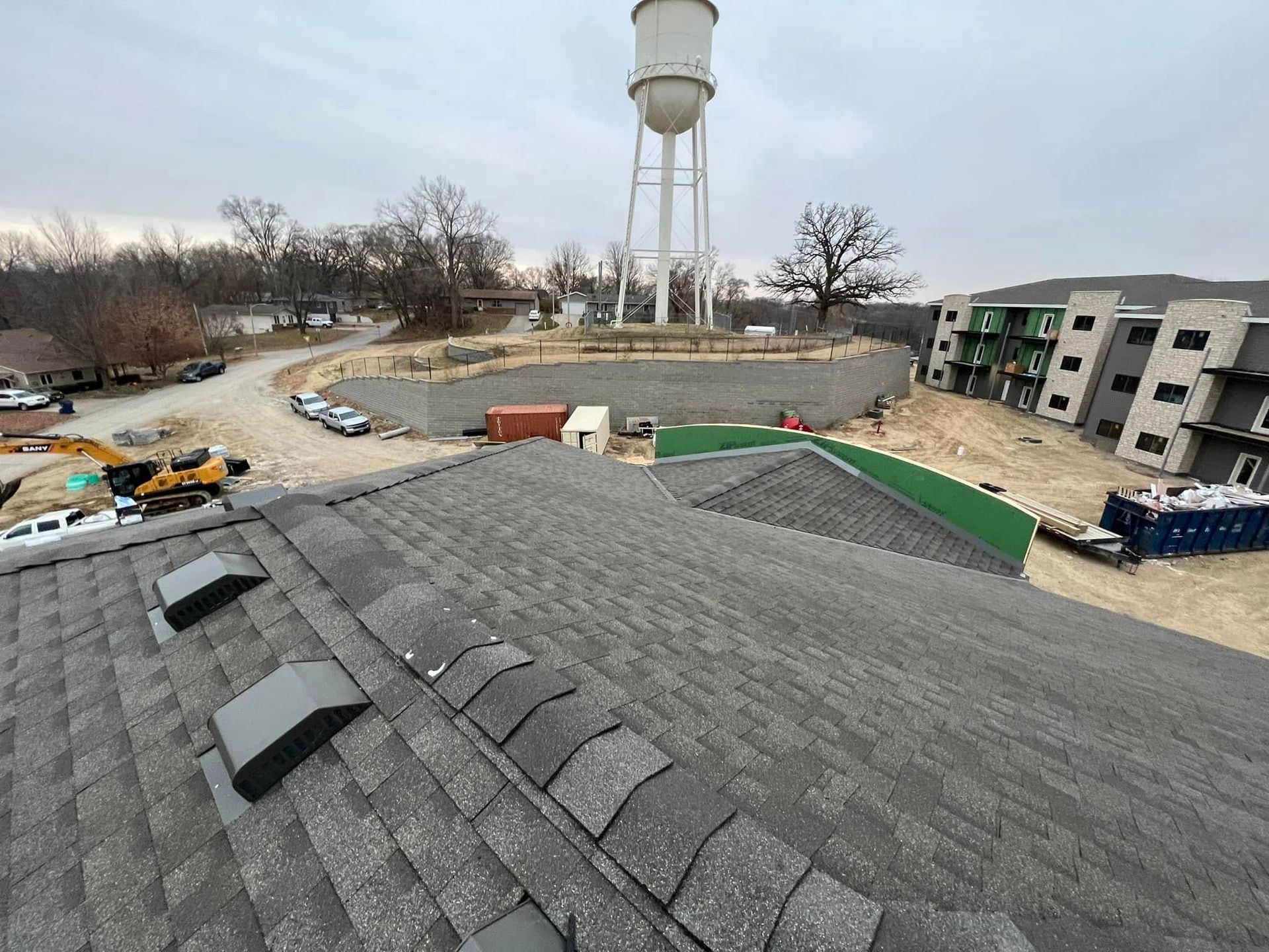 Rooftop view of a water tower, parking lot, and nearby apartment buildings under overcast skies