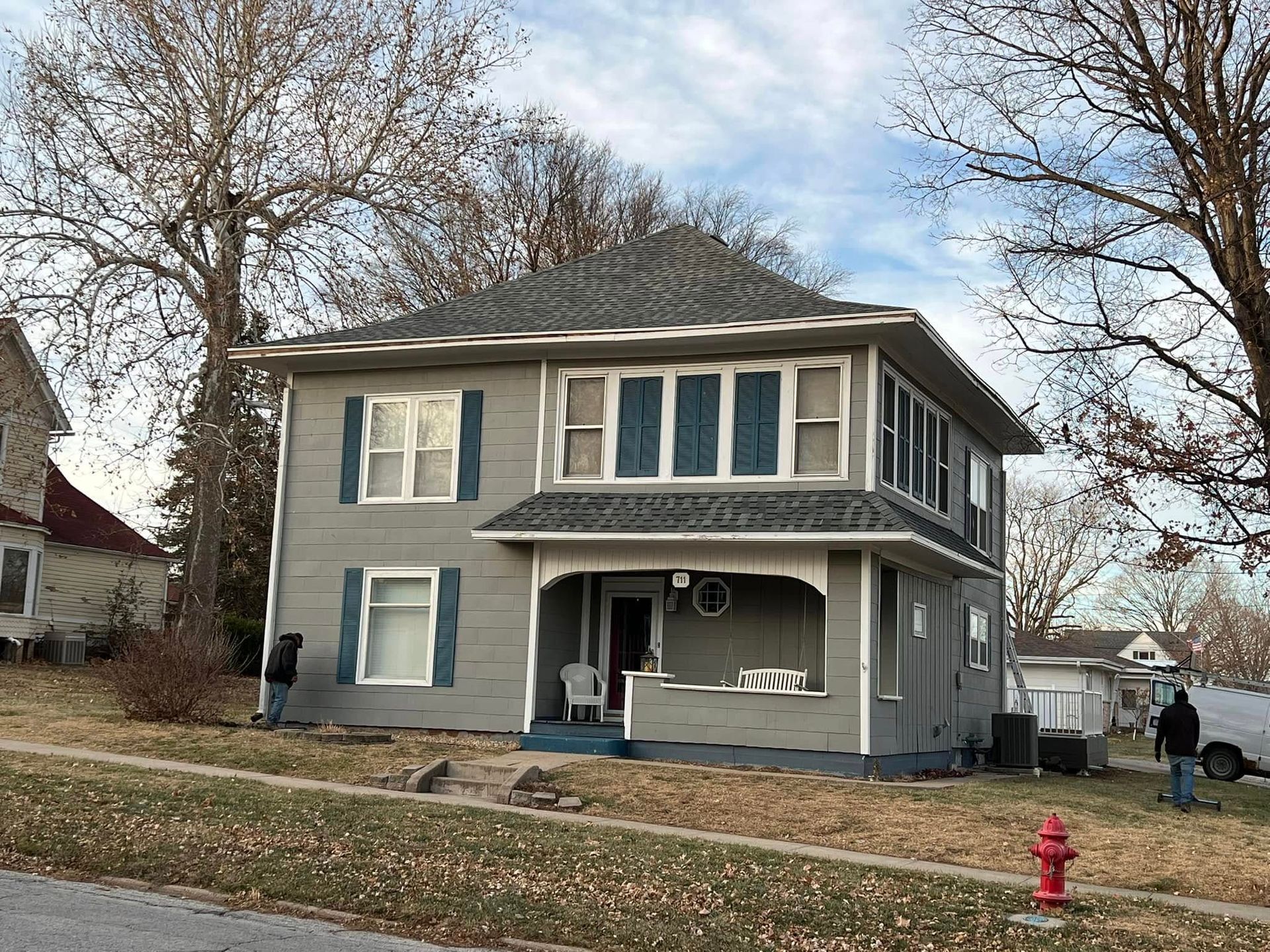 Two-story gray house with white trim and porch, winter trees, and a red fire hydrant in front