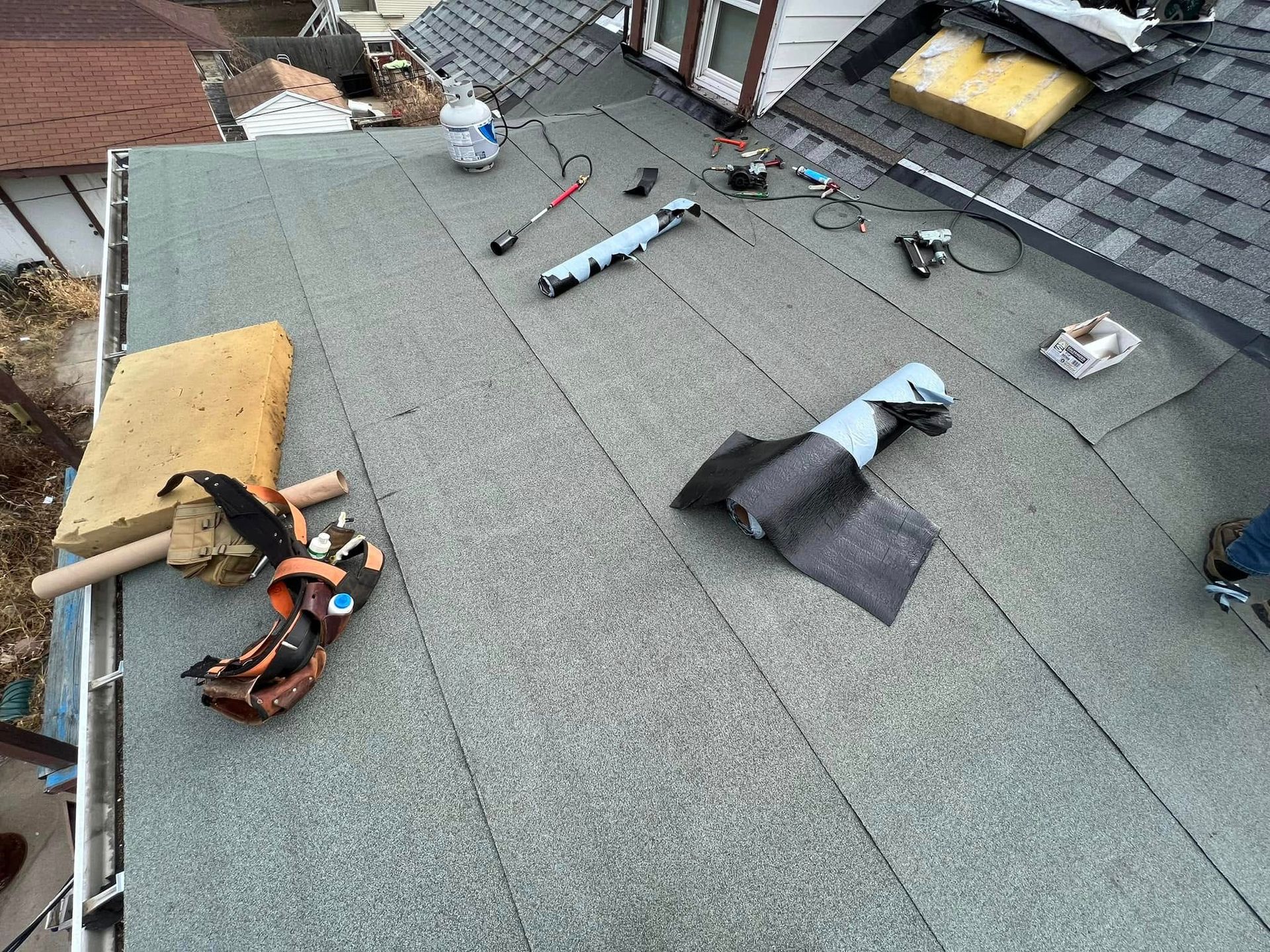 Roofing tools and materials scattered on a gray shingled roof during repair work
