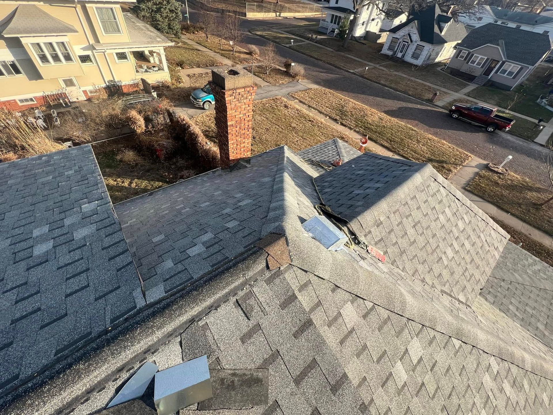 Rooftop view of gray shingled roofs and a brick chimney in a suburban neighborhood