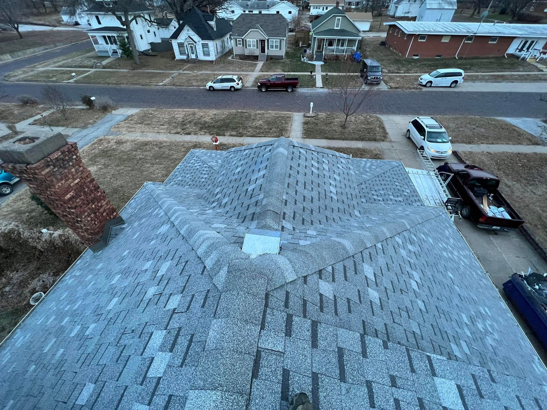 Rooftop with a freshly shingled section and nearby parked vehicles on a residential street