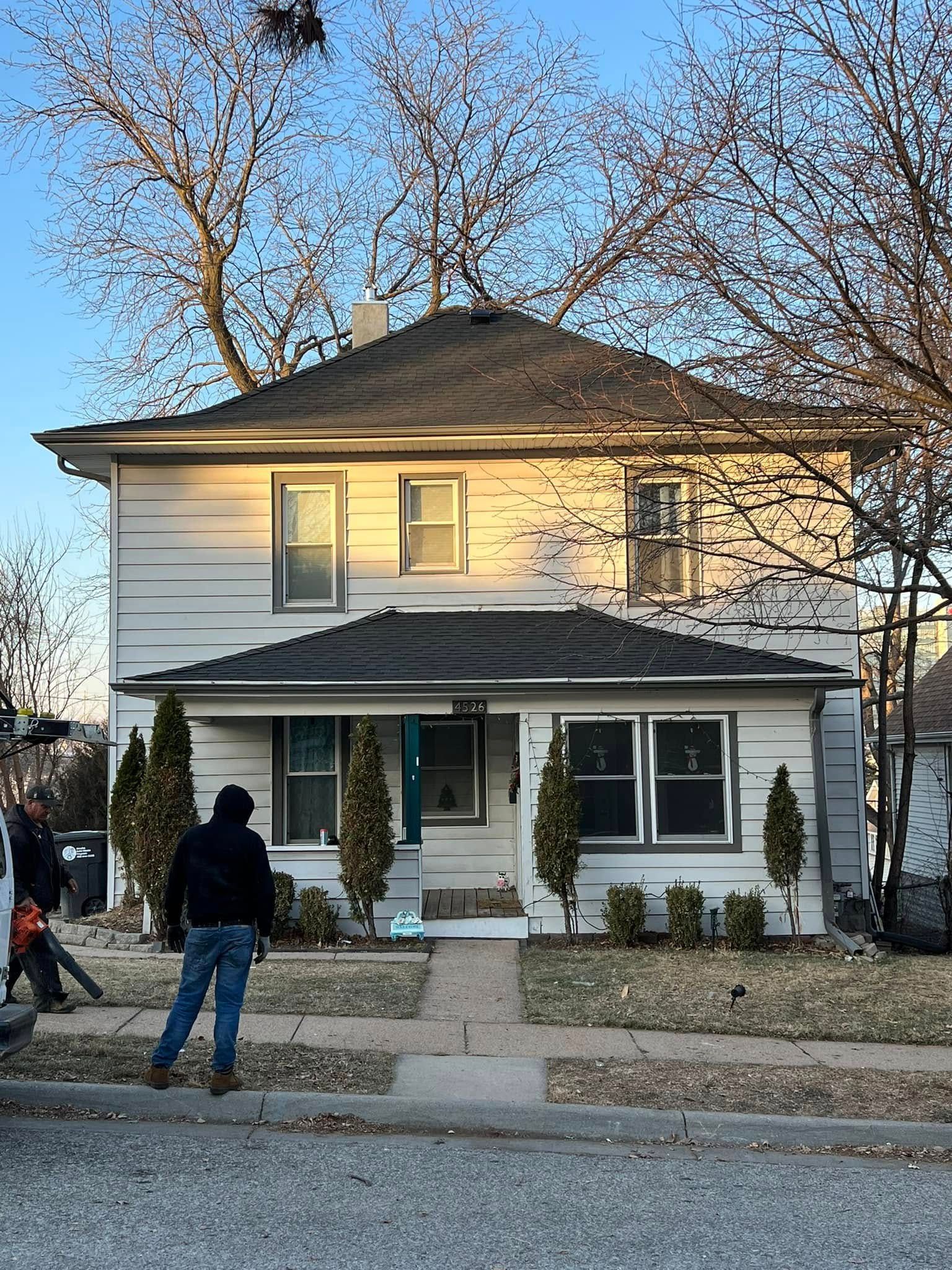 Two-story white house with porch, evening light, and two people standing on the sidewalk.