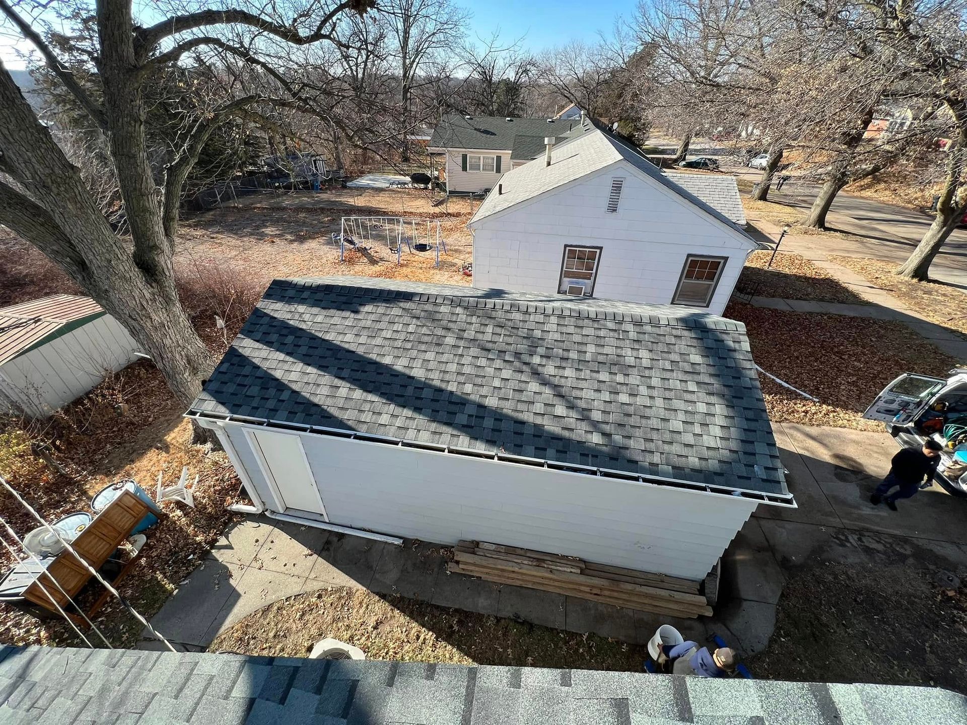Aerial view of a small white house with gray roof in a yard, with a person near the back fence.