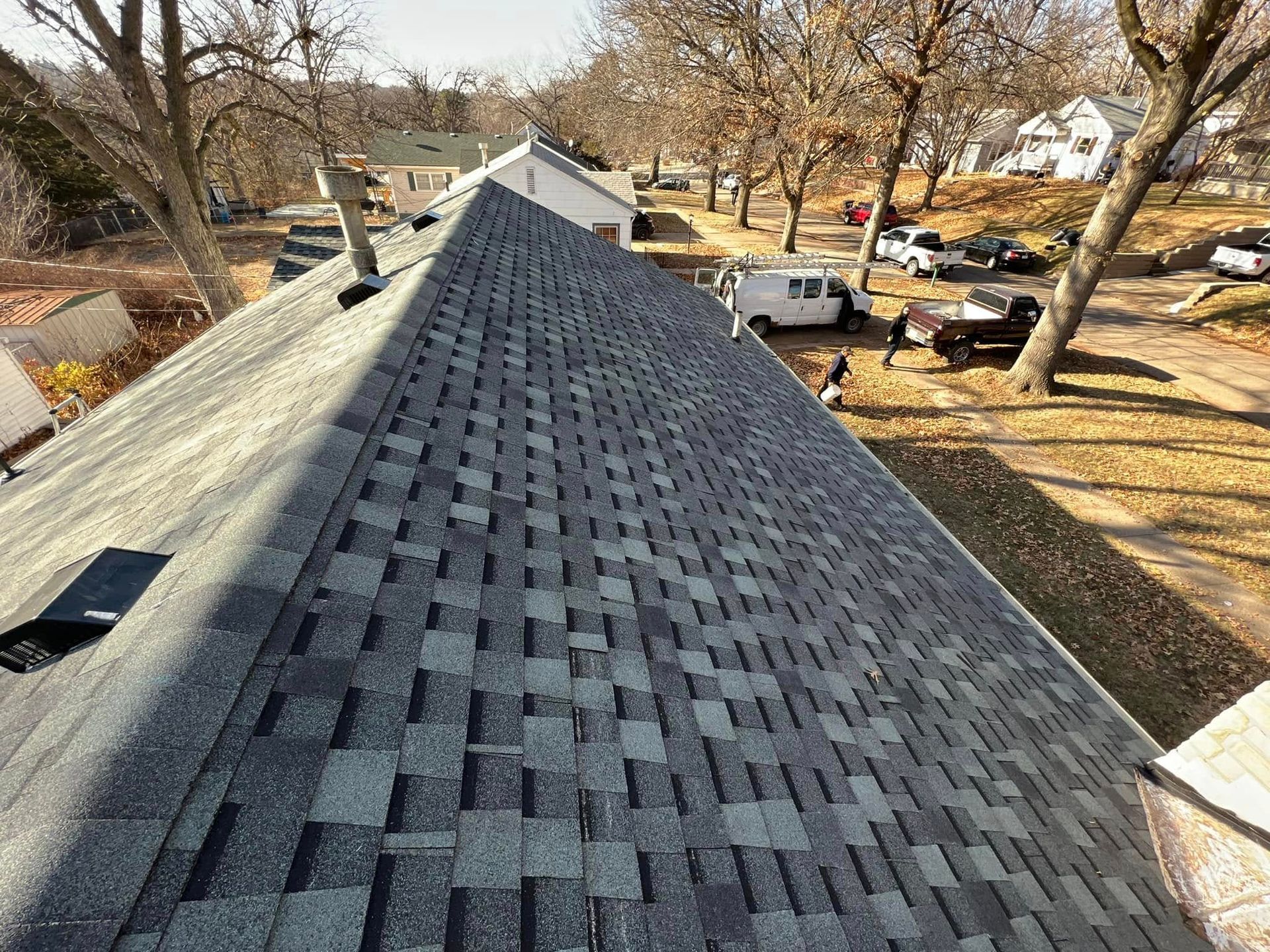 Roof covered with dark gray asphalt shingles, viewed from above on a residential street
