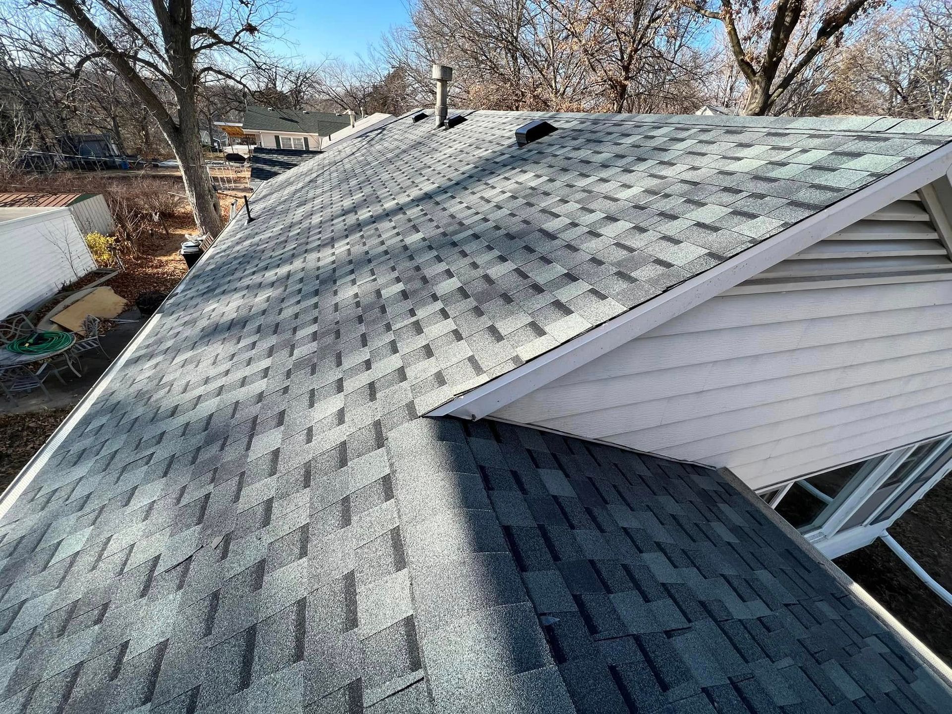 House roof with gray shingles and a dormer, viewed from above on a sunny day