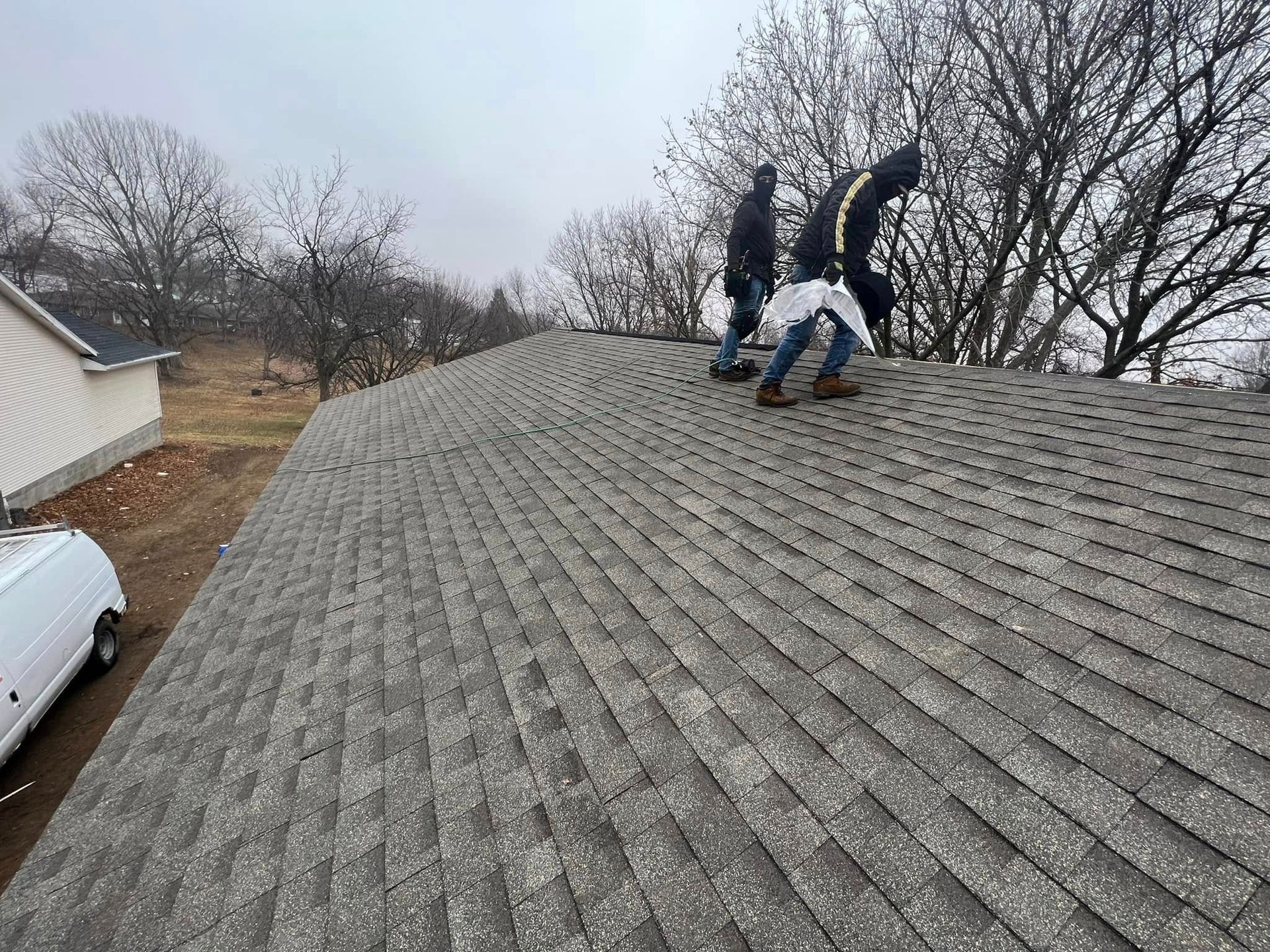 Workers on a shingled roof near a house, repairing near the ridge on an overcast day