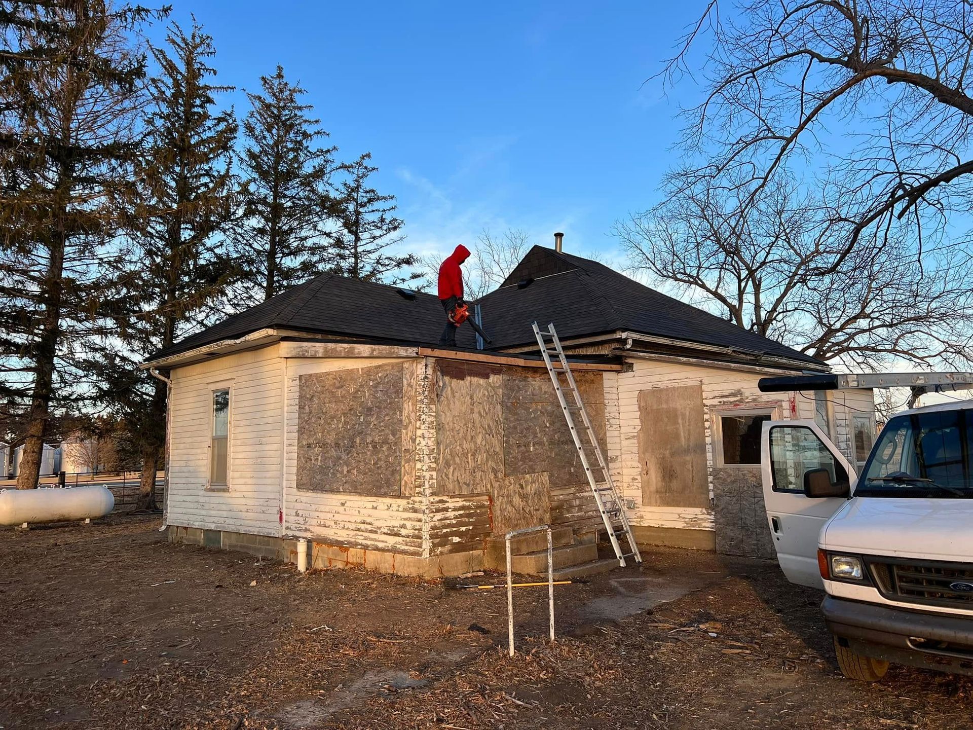 House roof repair with a worker in red on the roof and a ladder leaned against the house