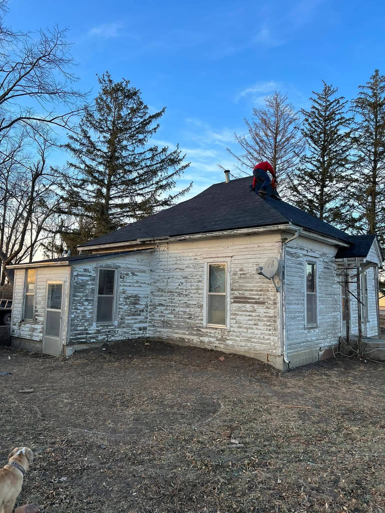 Old white brick cottage with dark roof and red chimney in a leaf-covered yard under blue sky