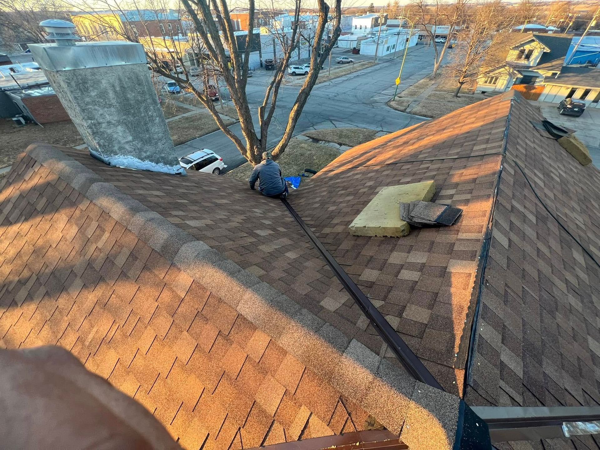 Roofers repairing a shingled roof beside a tree and chimney in daylight