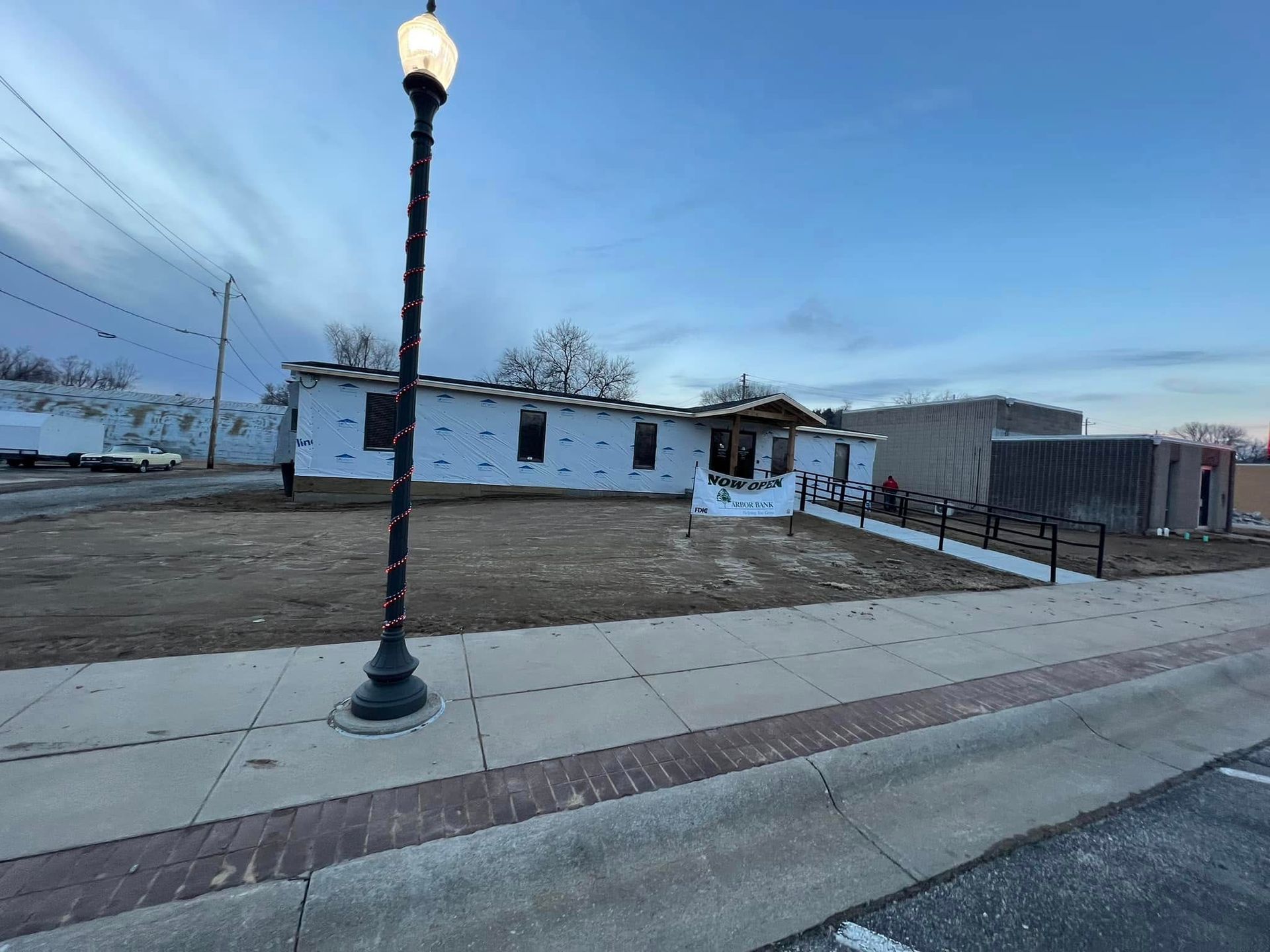 Snowy street corner with a lamppost, sidewalk, and a small building under a cloudy evening sky