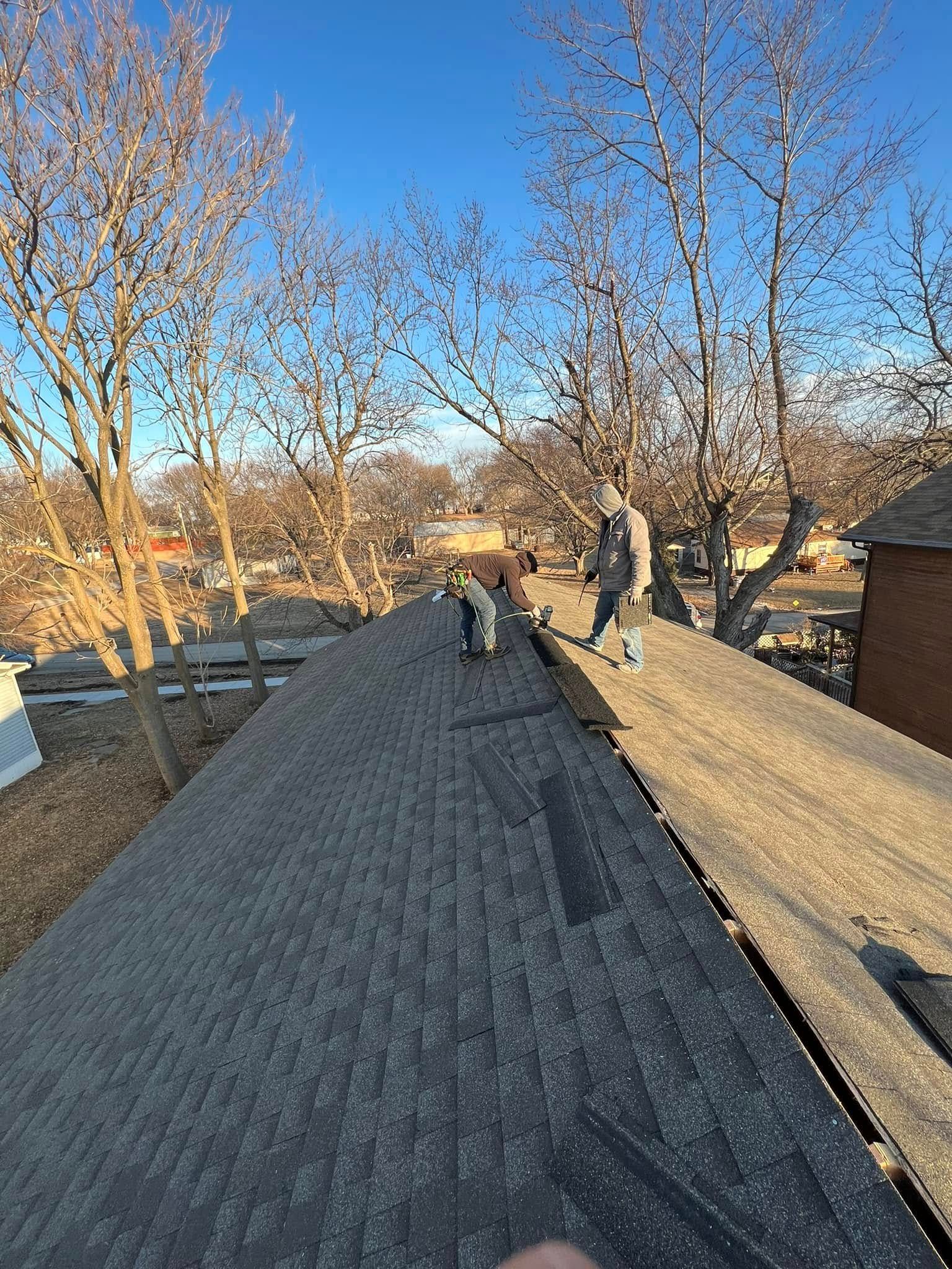Workers on a rooftop under a clear blue sky, with leafless trees and houses in the background