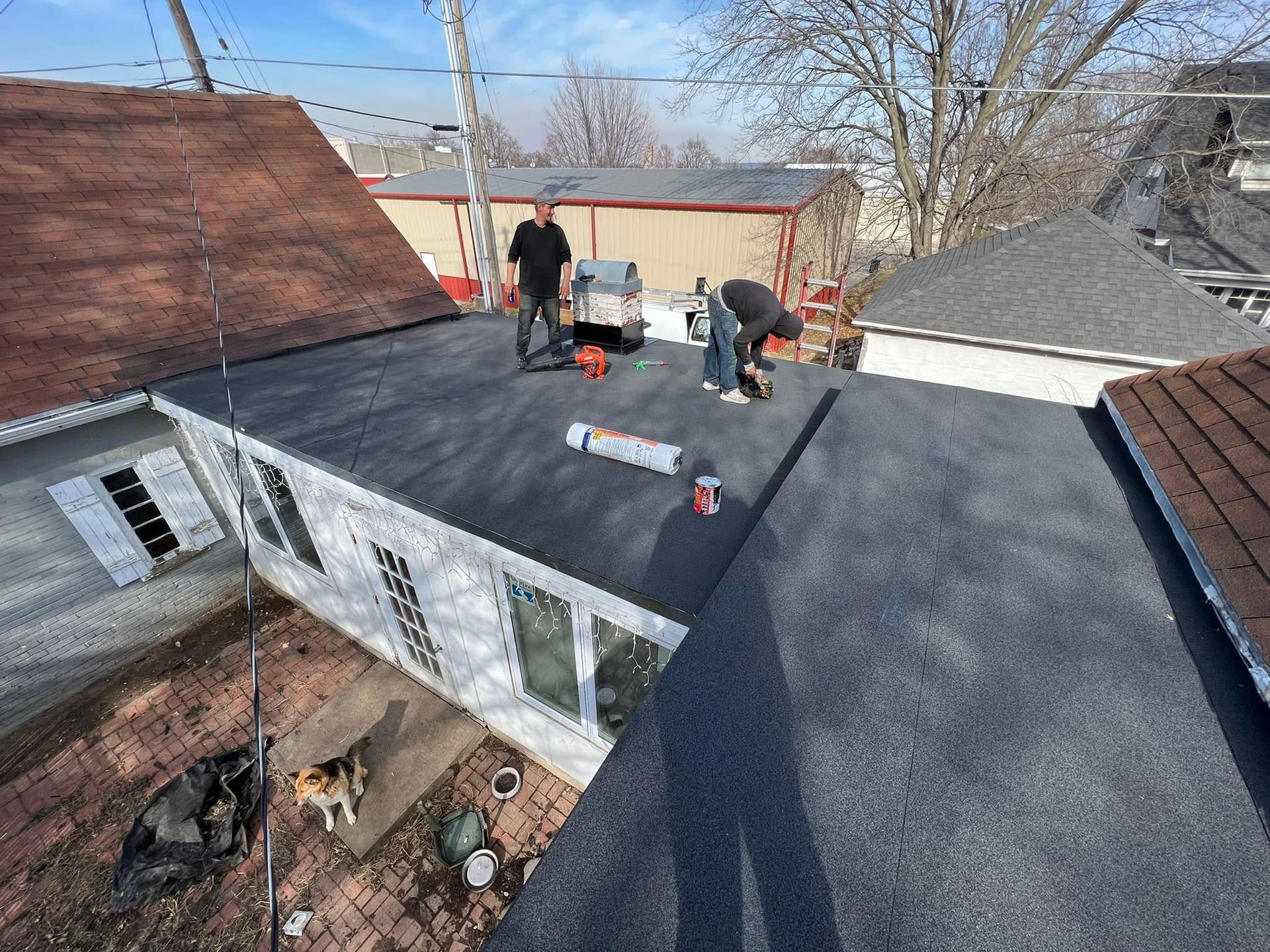 Workers repairing a black shingle roof on a house, with tools and materials spread across the rooftop.