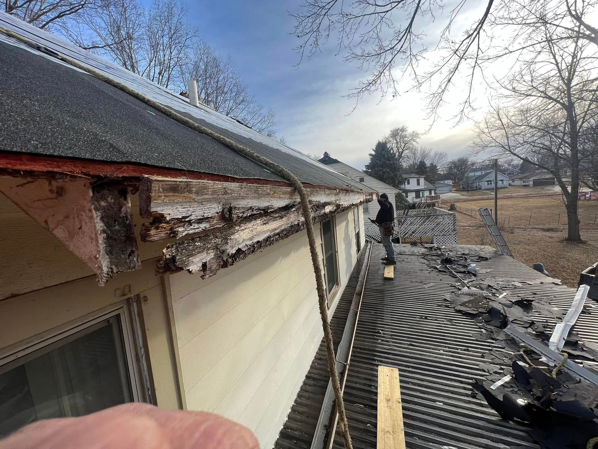 Damaged roof with peeled siding and debris, worker standing on a rooftop after storm damage.