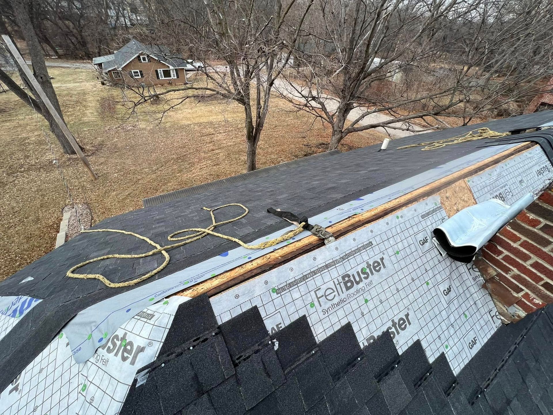 Damaged shingle roof with exposed underlayment and scattered debris in a wooded yard