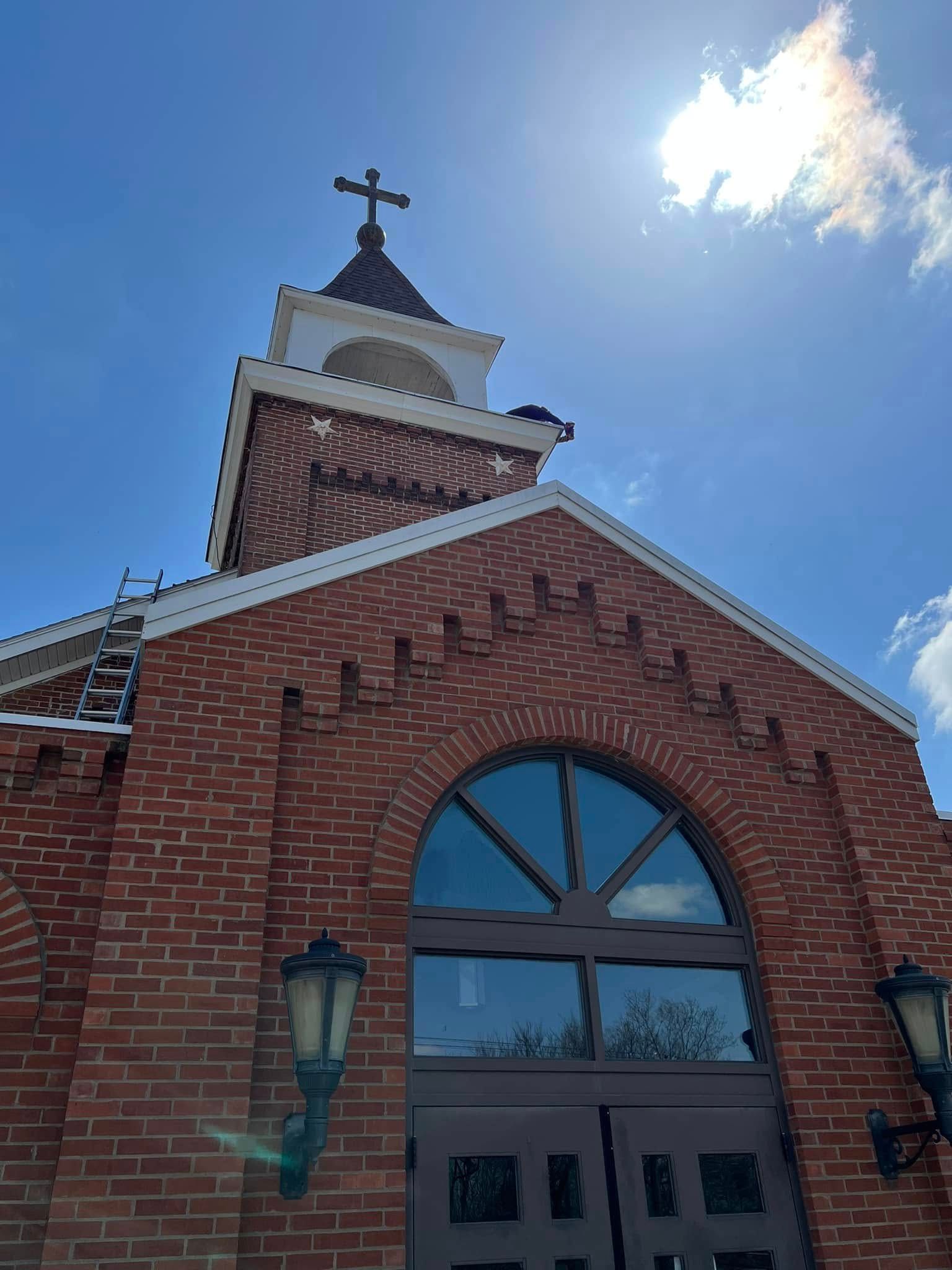 Brick church facade with arched window, steeple cross, and bright blue sky