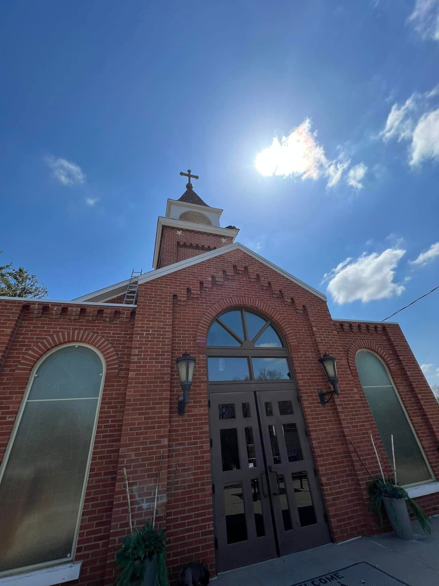 Red brick church entrance with arched windows and a small steeple under a bright blue sky