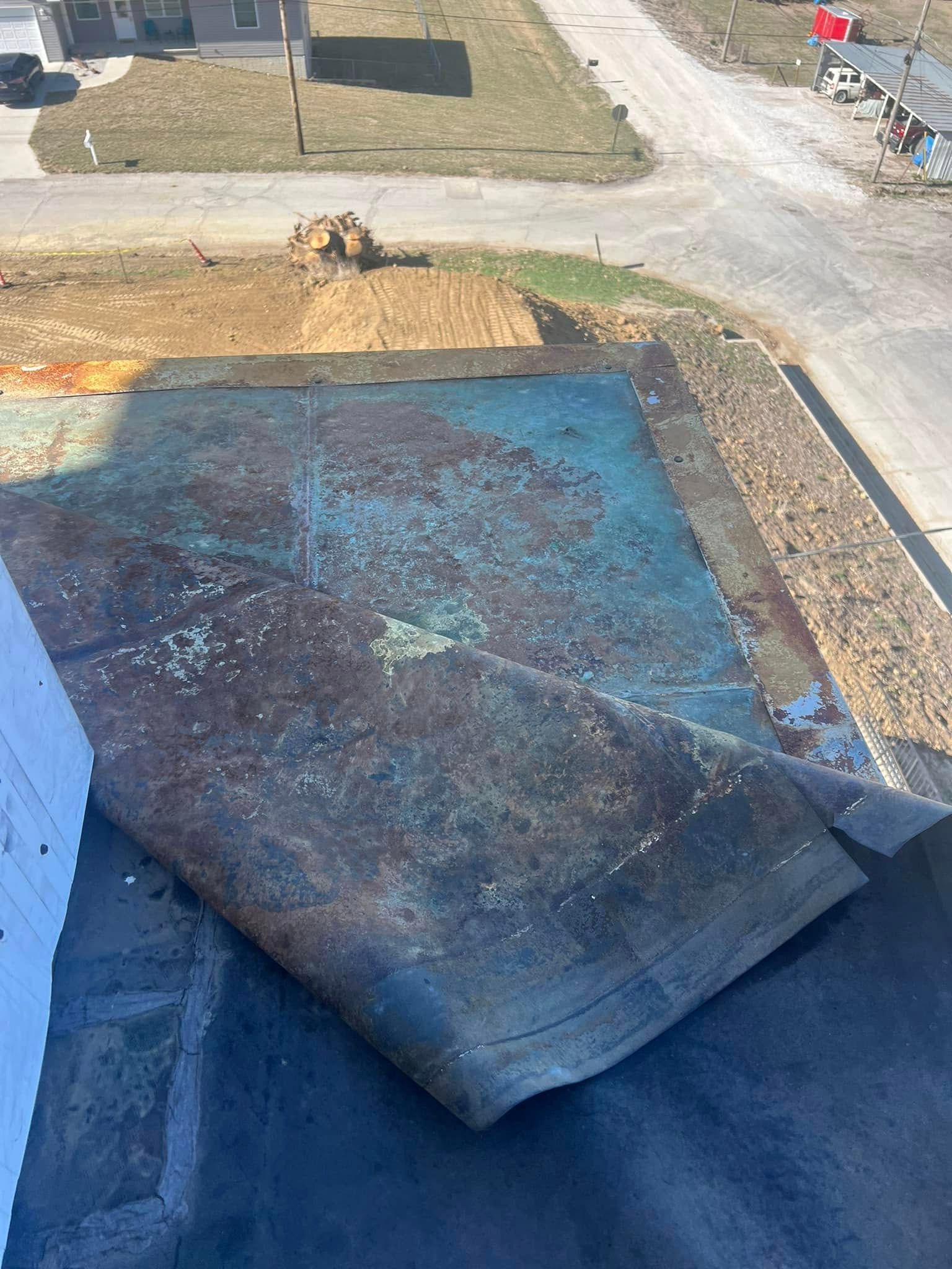 Blue tarp covering a roof edge beside a gravel road and yard, with a rolled tarp section in the foreground
