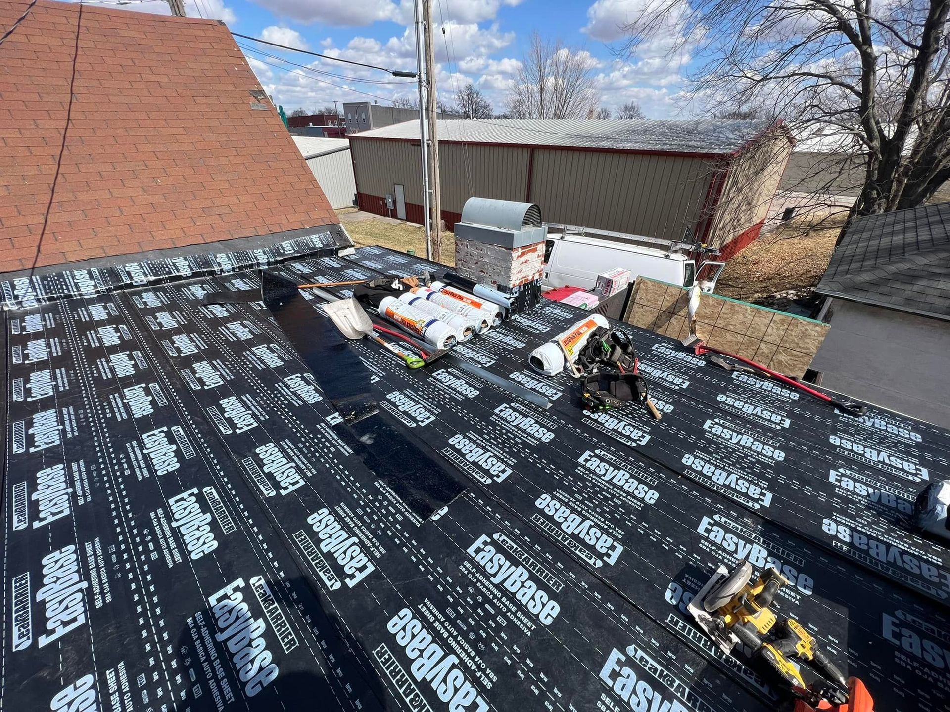 Roof under repair with black underlayment and scattered tools on a sunny residential house