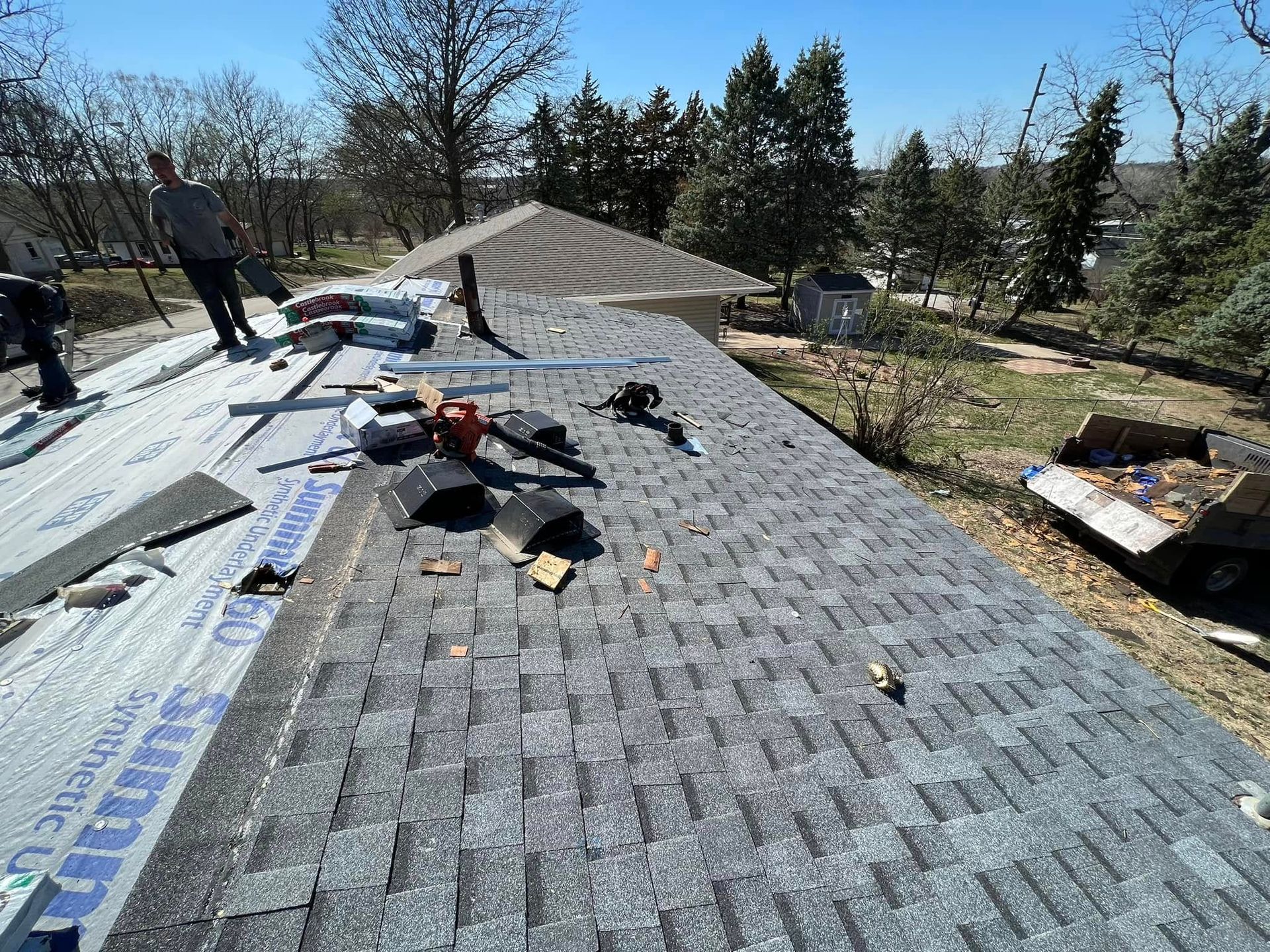 Workers installing gray shingles on a sloped roof in sunny weather