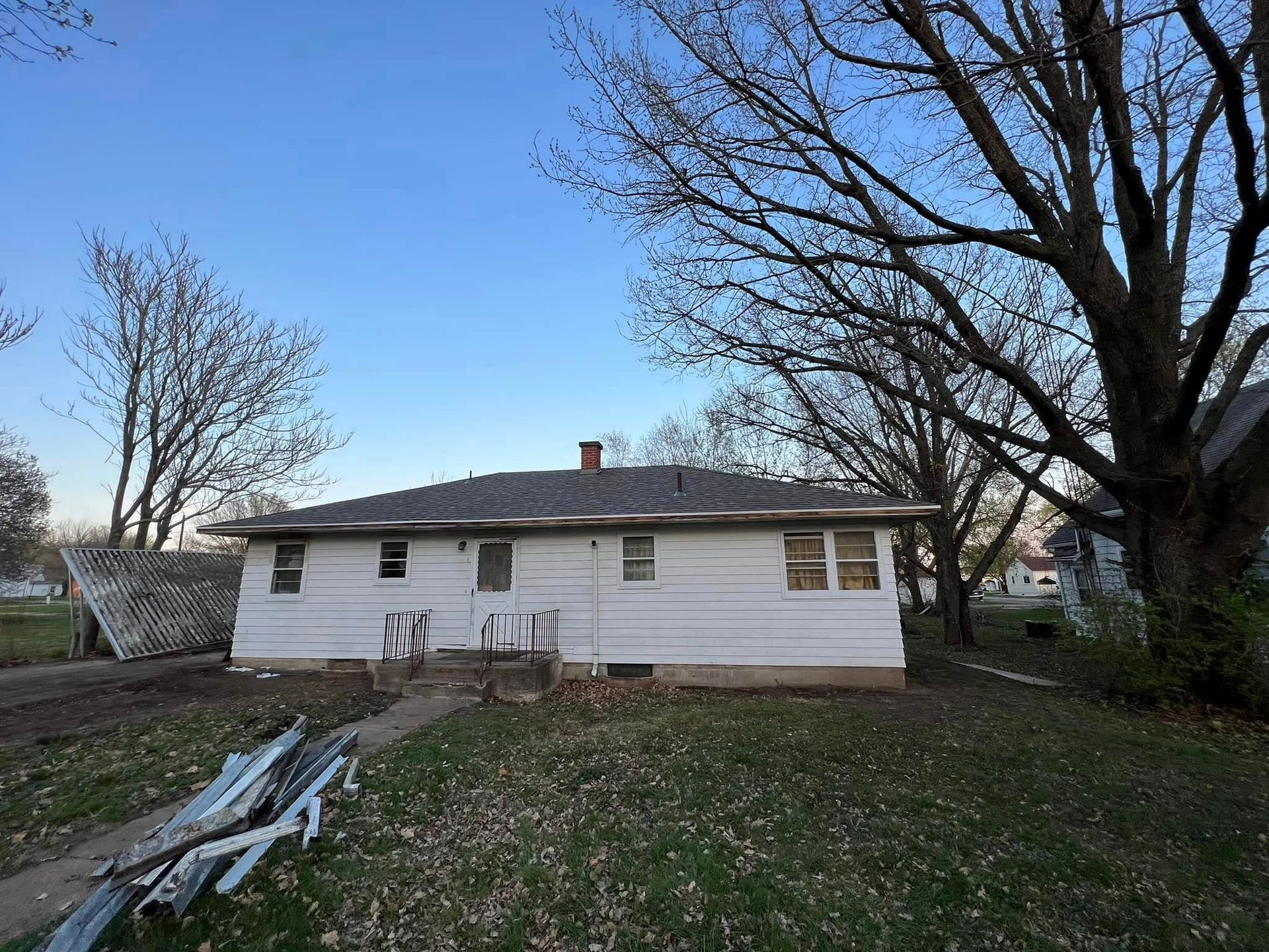White single-story house with damaged siding and scattered boards in a yard under bare trees