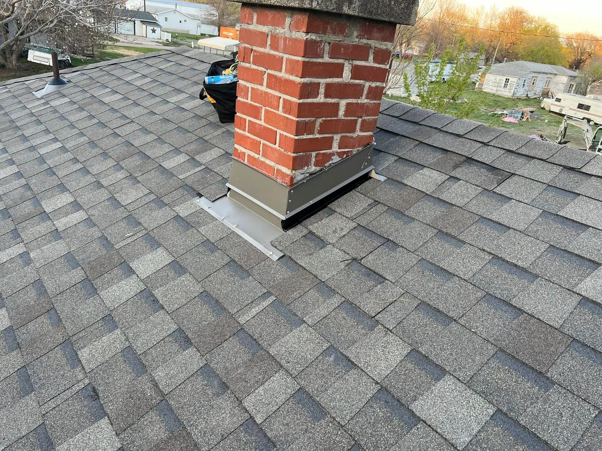 Rooftop with gray shingles and a red brick chimney, viewed from above.