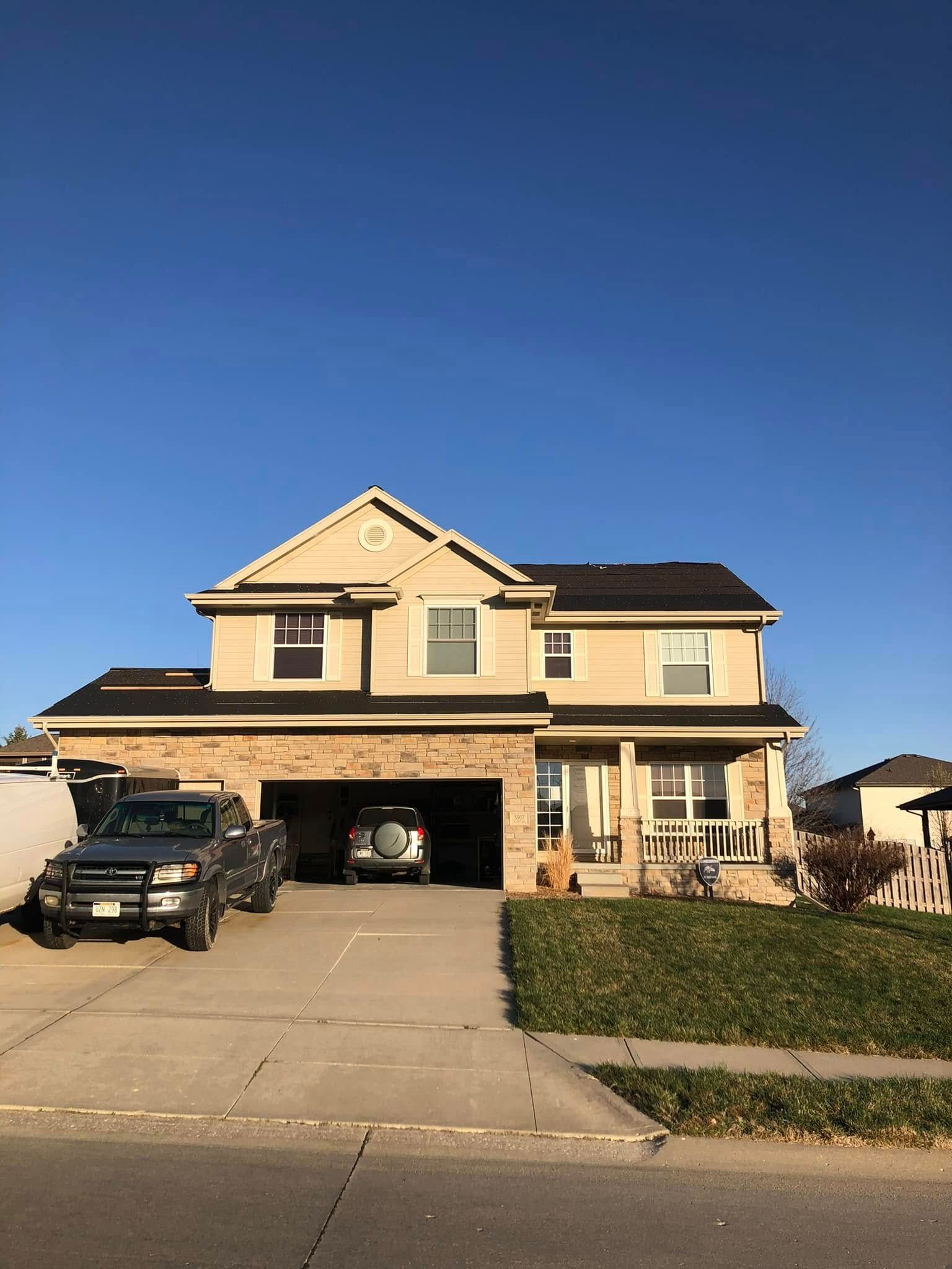 Suburban two-story house with a driveway, parked SUV, open garage, and clear blue sky.
