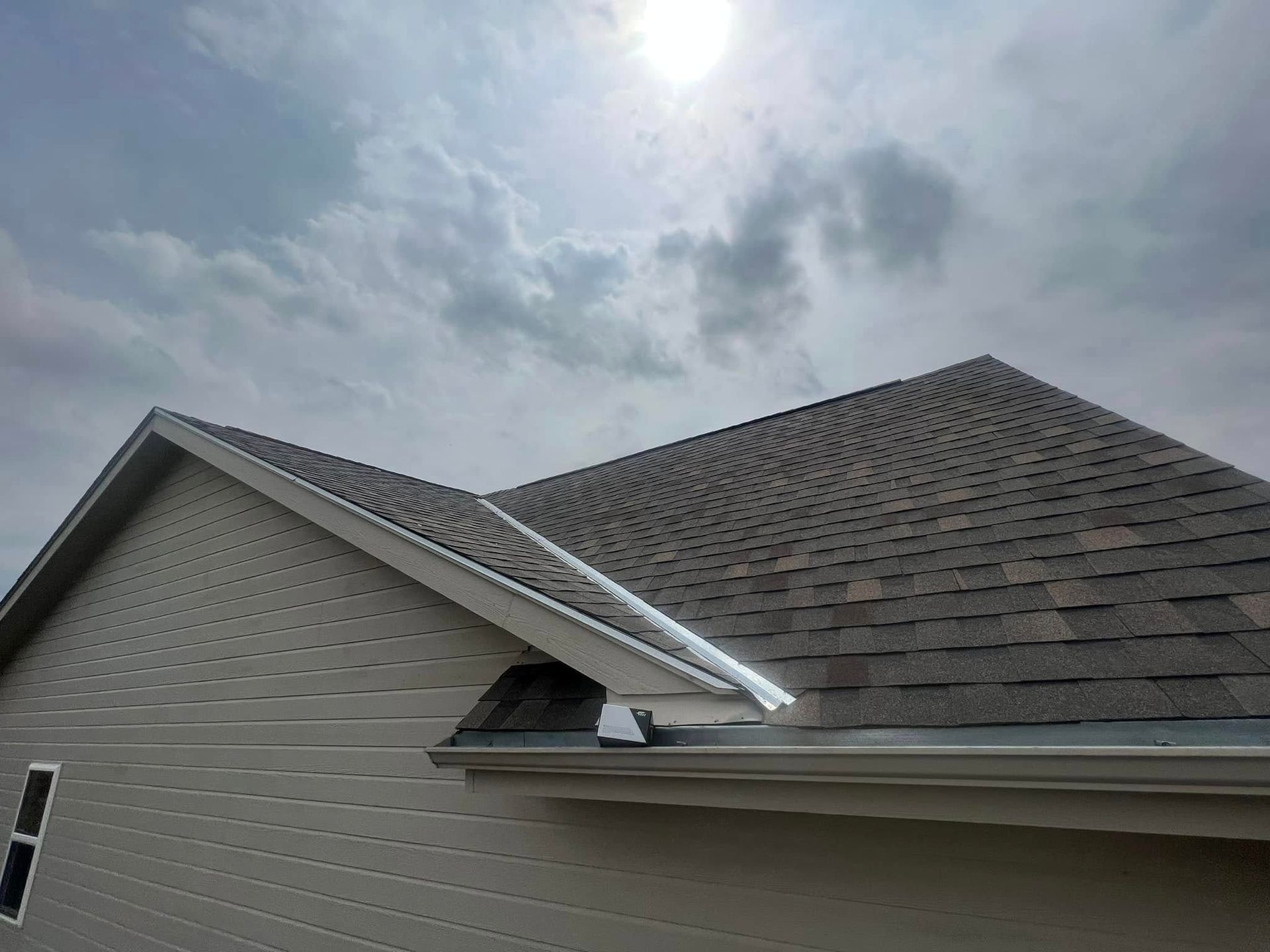 House roof under a cloudy sky with the sun shining overhead