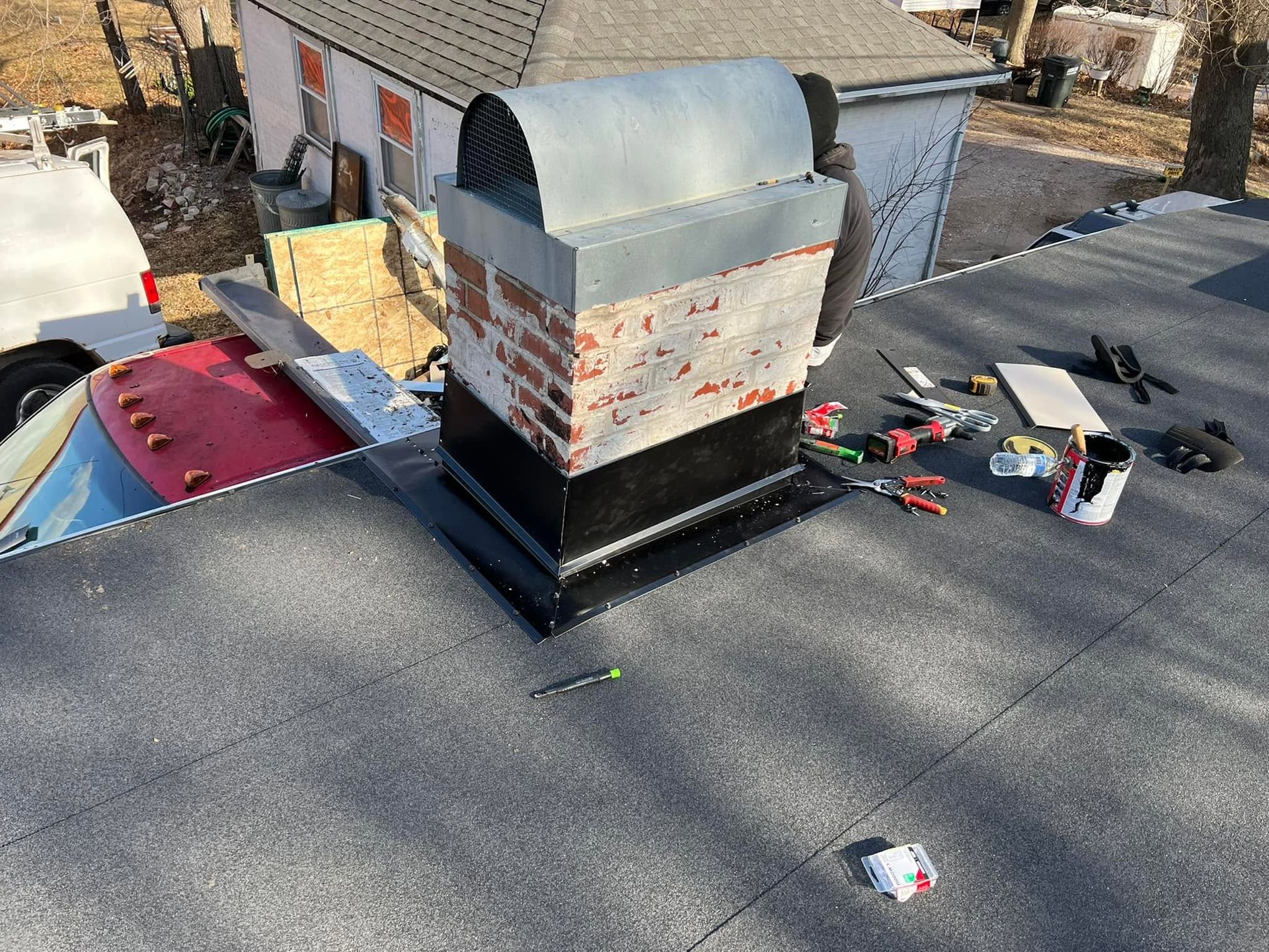Rooftop chimney with metal cap, surrounded by shingles and scattered tools during repair work