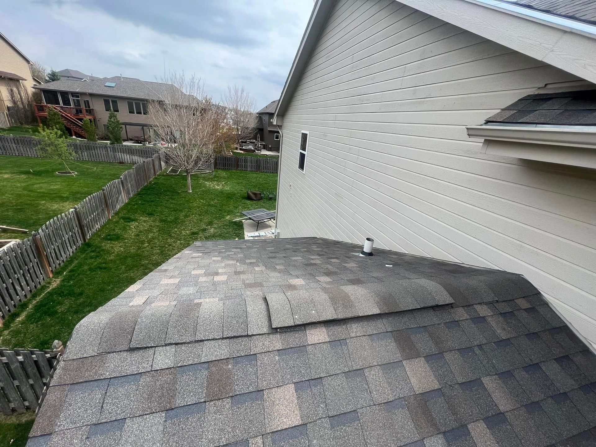 Backyard view of a house roof with gray shingles and white siding beside a grassy yard and fence
