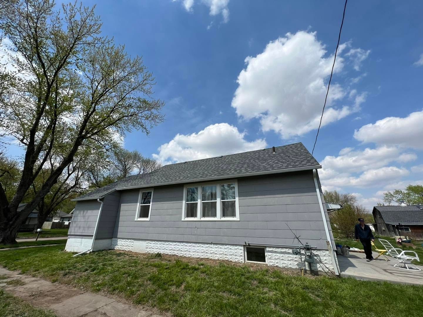 Gray house with new roof and white trim, viewed from the yard under a blue sky with clouds.