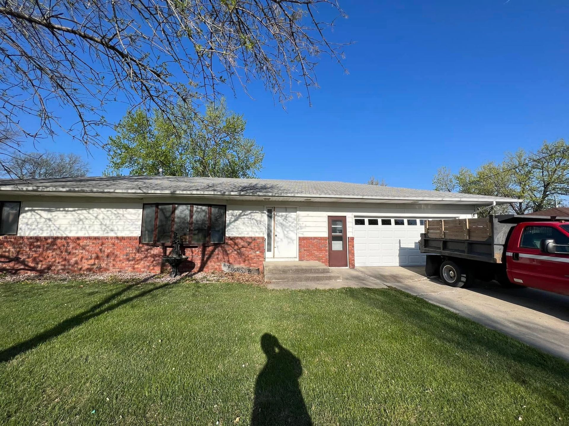 Single-story brick house with white garage door, red truck in driveway, and sunny front lawn.