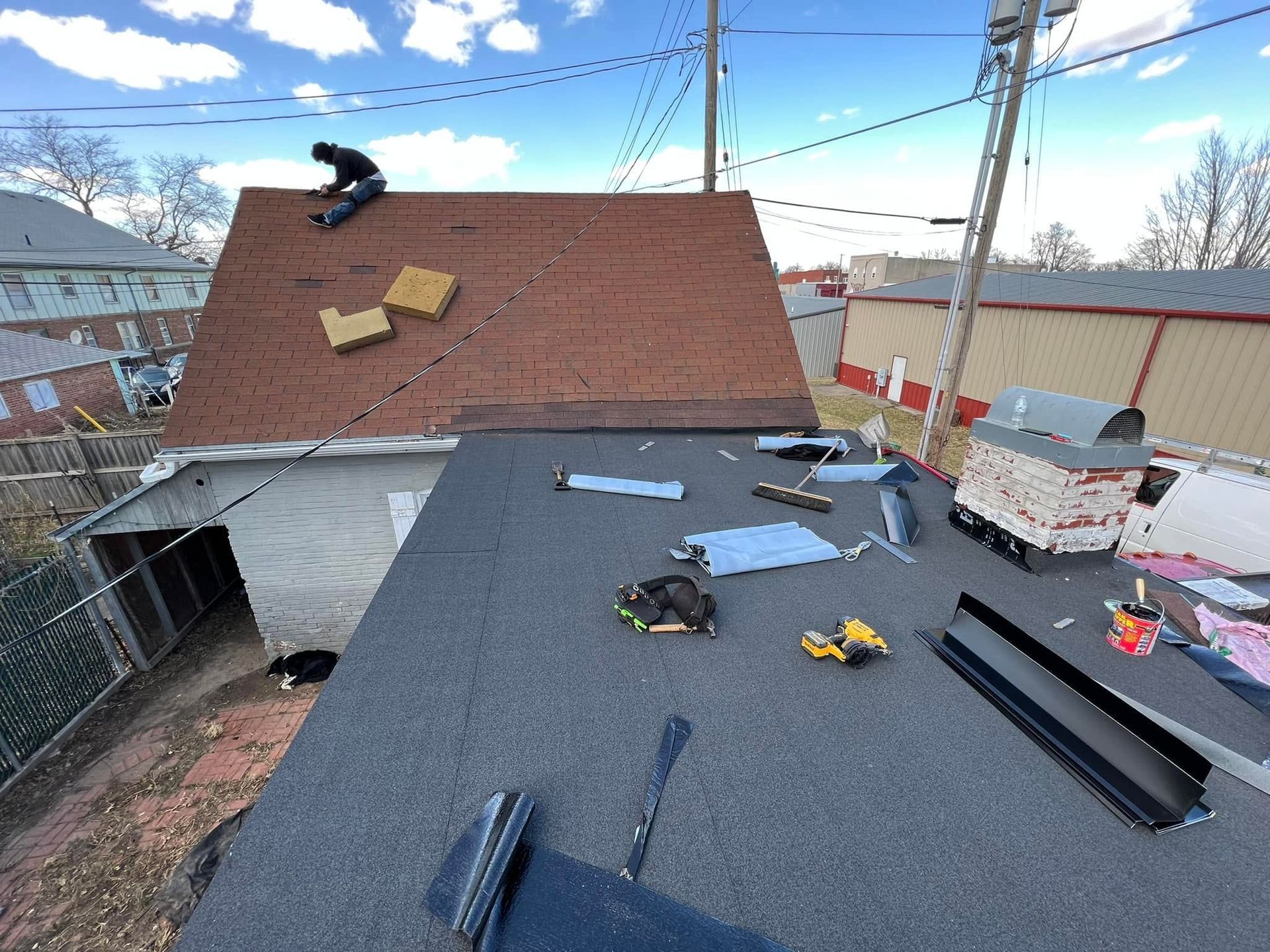 Two workers roofing a house, with shingles and tools scattered on the roof under a blue sky.