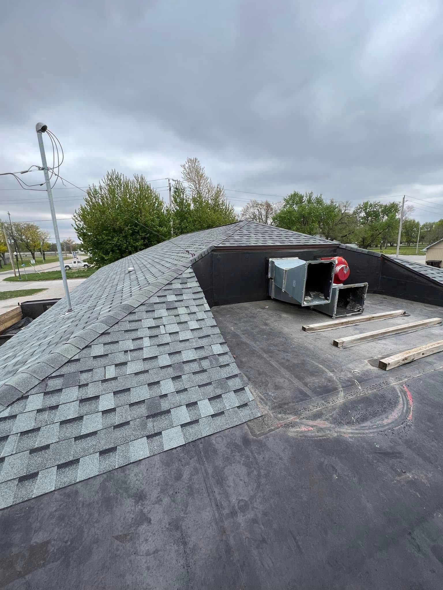 Roofer on a shingled roof beside an HVAC unit under cloudy skies