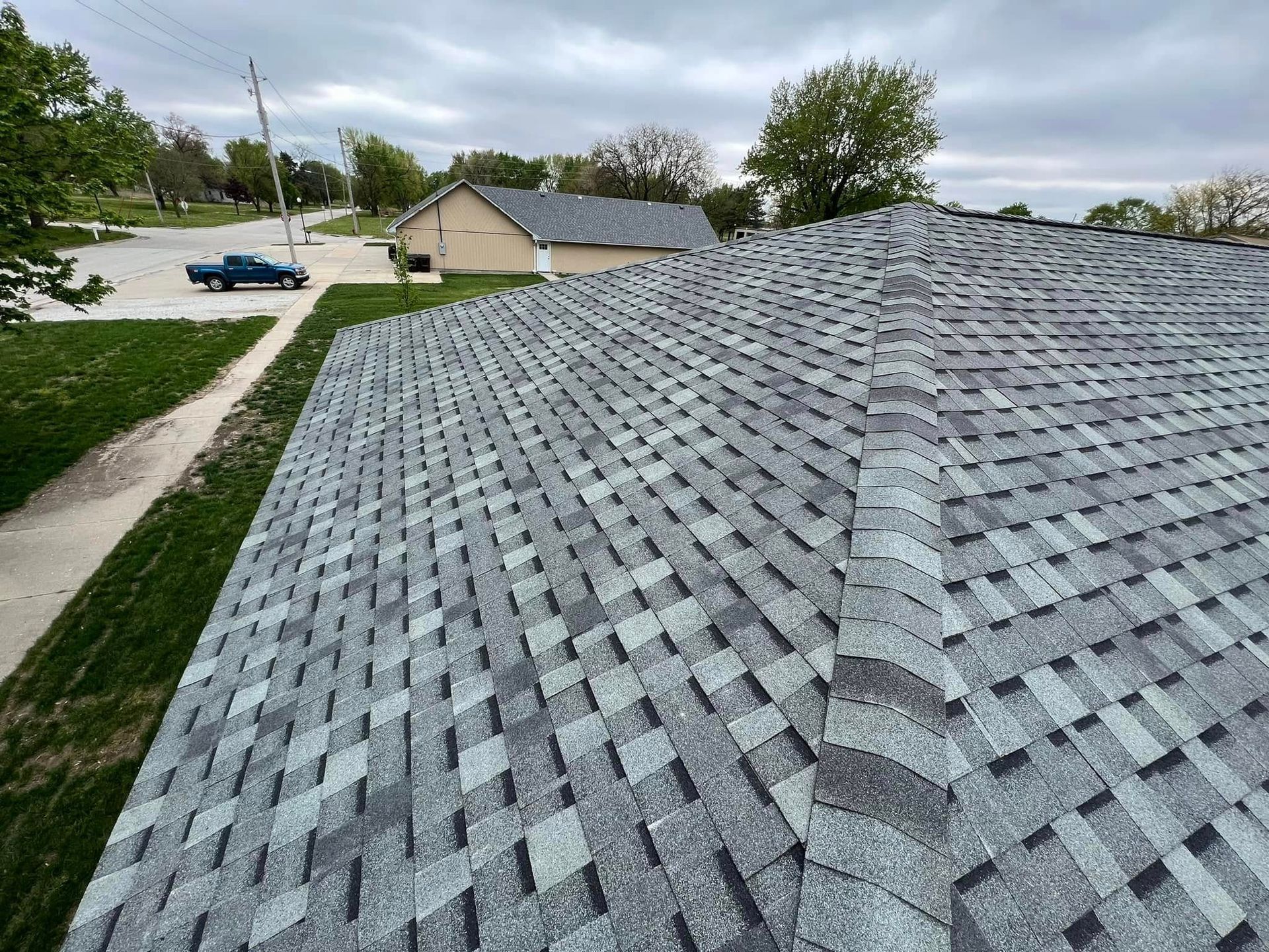 Gray shingled rooftop overlooking a suburban street and houses on a cloudy day