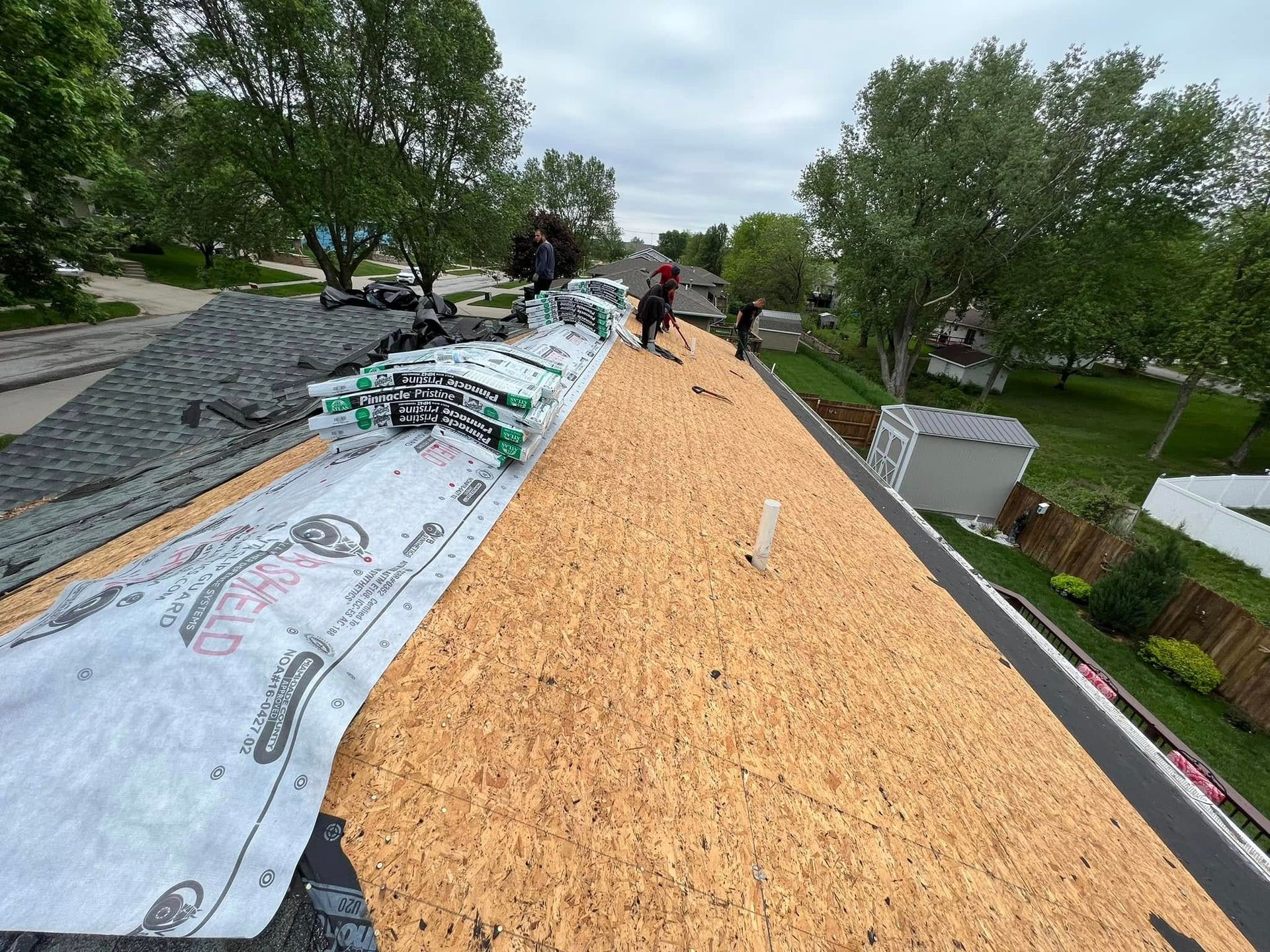 Roofers installing underlayment and orange roof decking on a steep roof under cloudy skies.