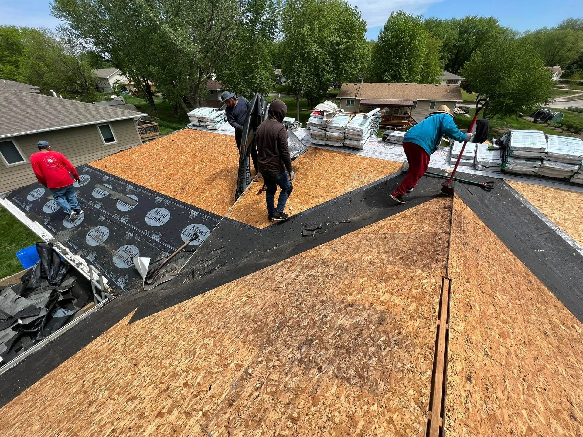 Workers installing shingles on a roof, with black underlayment and wood decking visible.