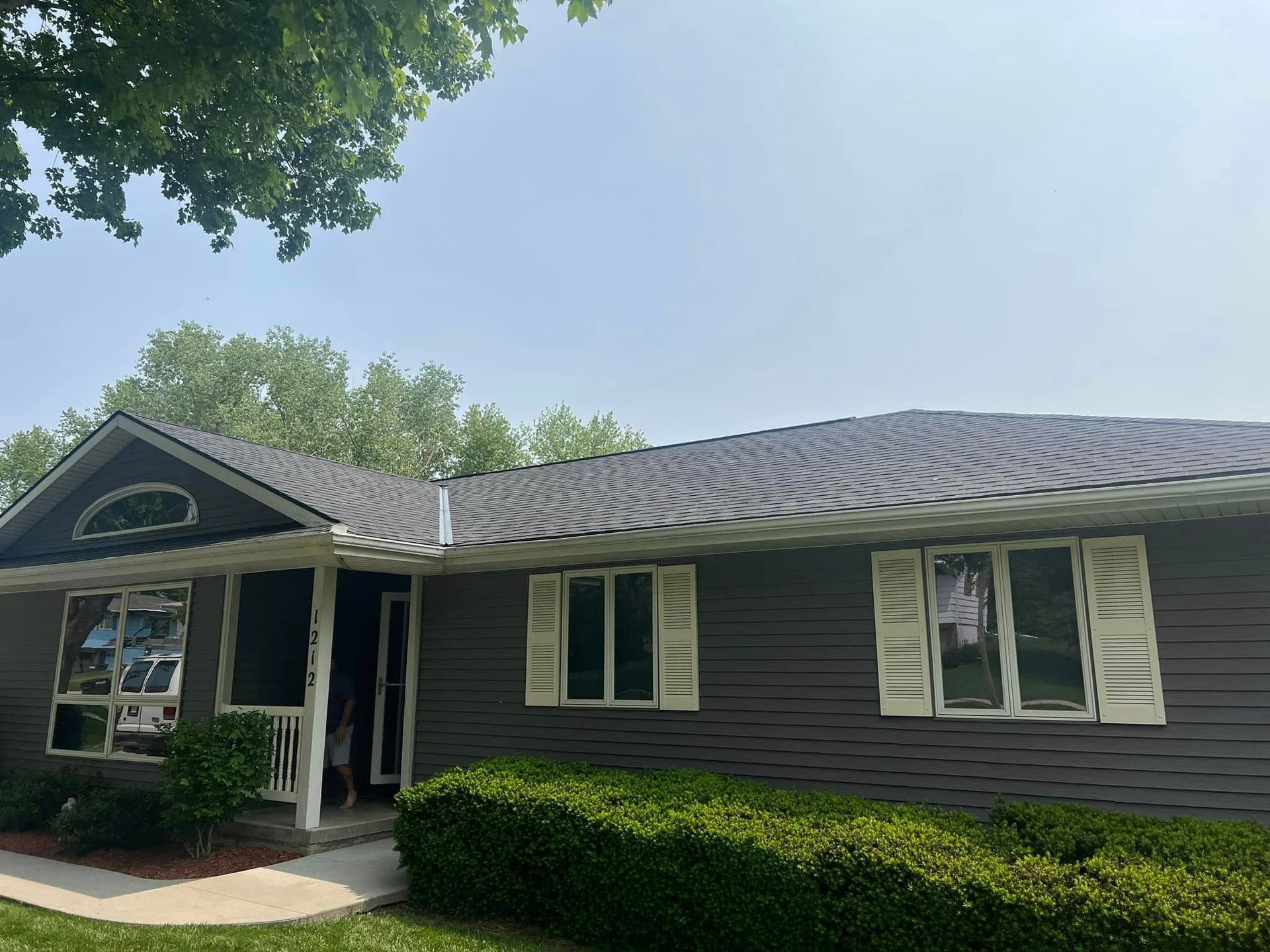 Single-story dark gray house with white trim, front porch, and neatly trimmed hedges under a blue sky