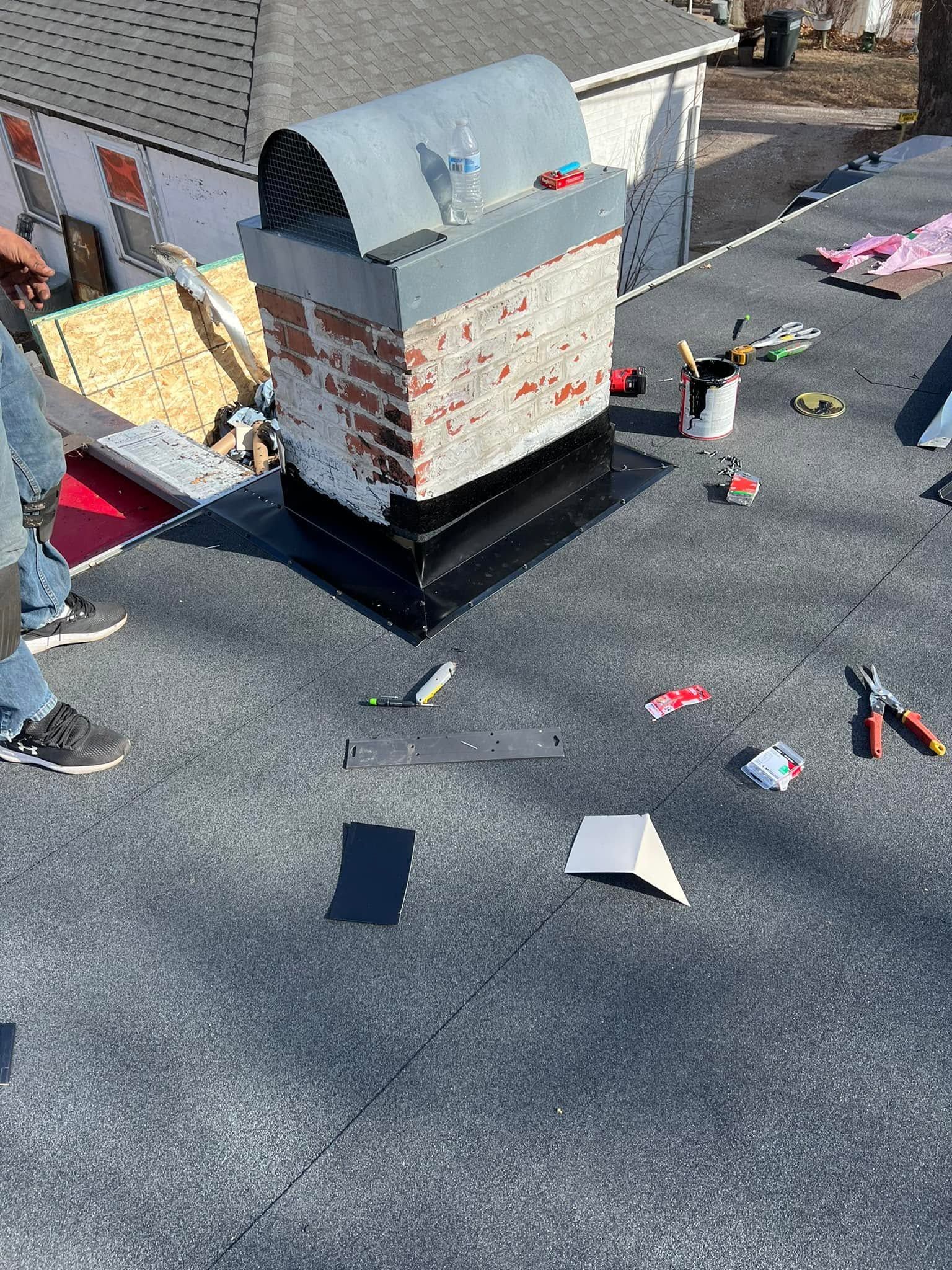 Rooftop work area with a small metal structure, scattered tools, and materials on gray shingles.